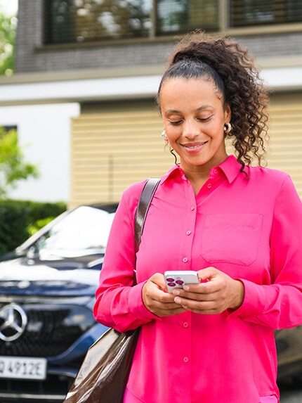 Een persoon staat voor een Mercedes-Benz voertuig en gebruikt haar&nbsp;mobiel apparaat.