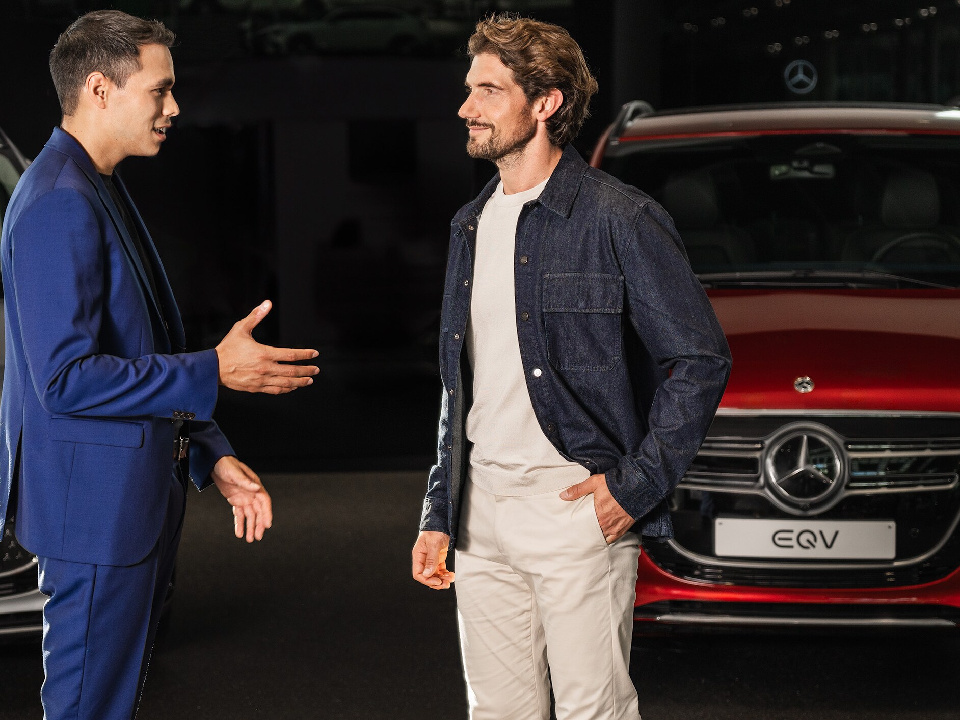Twee mannen praten in een Mercedes-Benz showroom voor een rode EQV