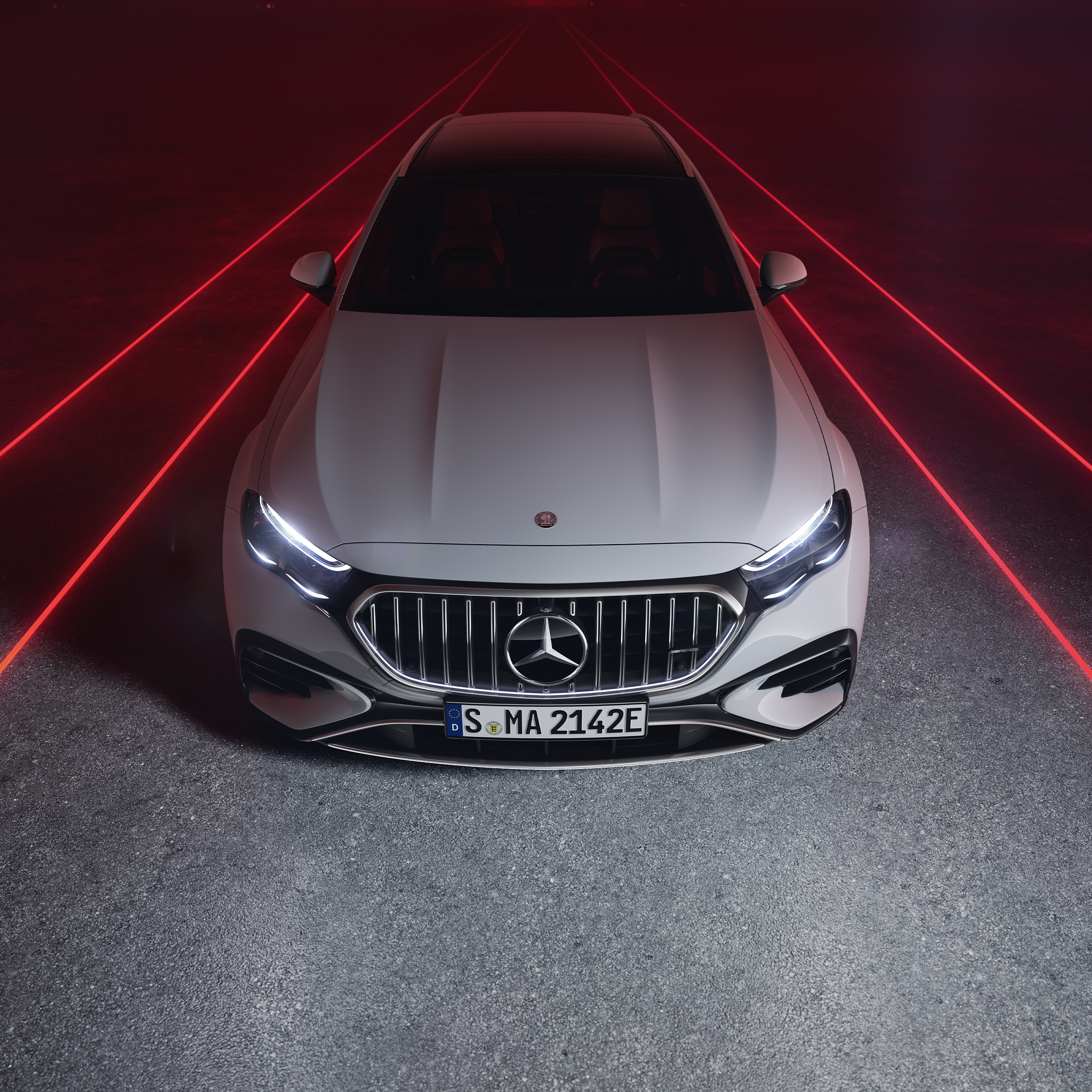 Vooraanzicht van de Mercedes-AMG E 53 HYBRID 4MATIC+ tegen een rode achtergrond, van bovenaf gezien.