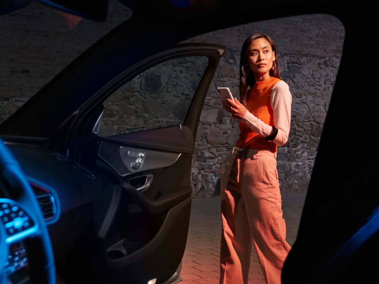 Er staat een persoon voor het geopende portier van een Mercedes-Benz EQ en deze persoon houdt een smartphone in de hand waarop de Mercedes me App is geopend.