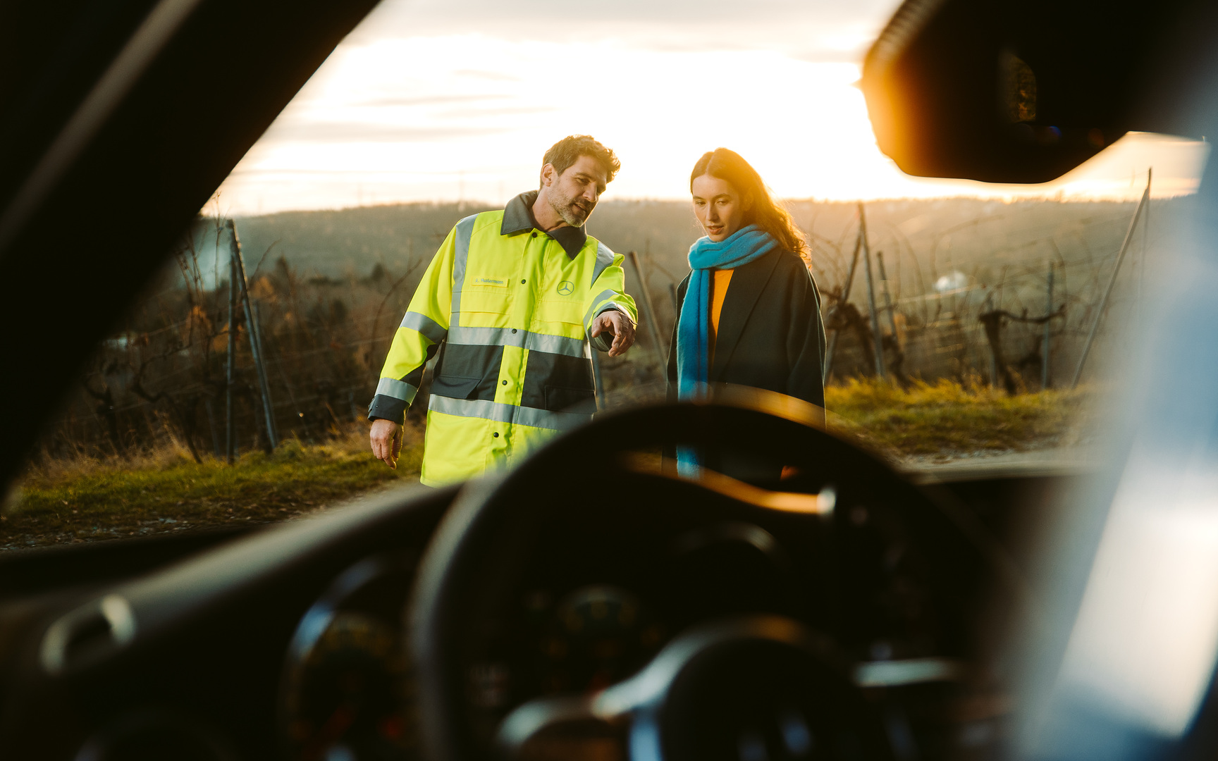 Hulp bij pech en schade | Mercedes-Benz Door de voorruit van een Mercedes-Benz zien we een servicemonteur die naast de bestuurder voor de auto staat en naar de voorruit wijst.