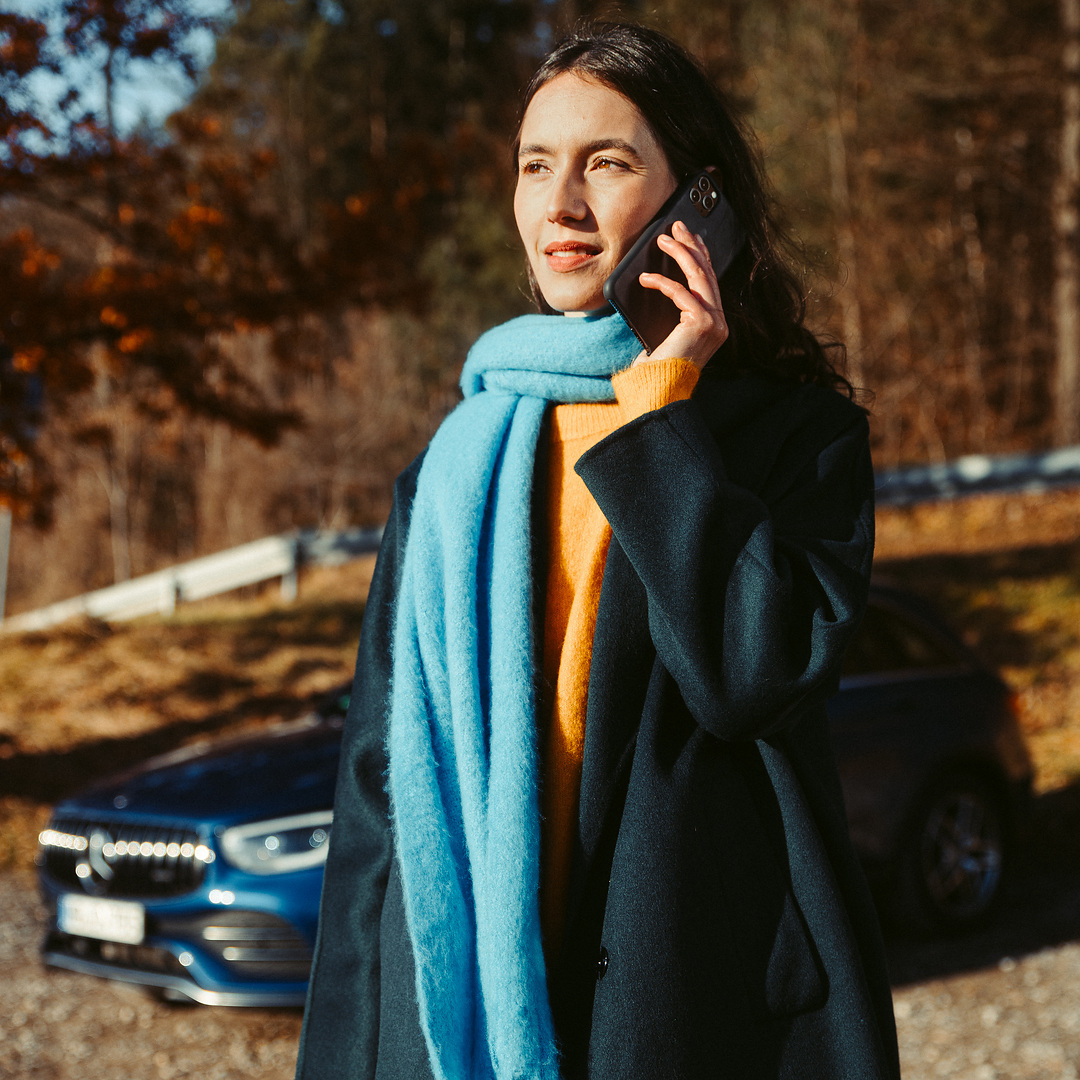 Hulp bij pech | Mercedes-Benz Een vrouw staat voor haar Mercedes SUV en telefoneert met een smartphone.