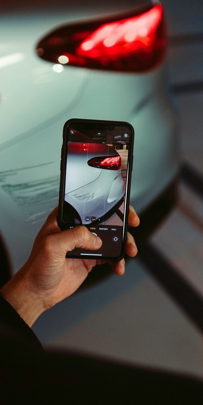 Een man fotografeert met een smartphone de schade aan het achterste spatscherm van zijn Mercedes-Benz.