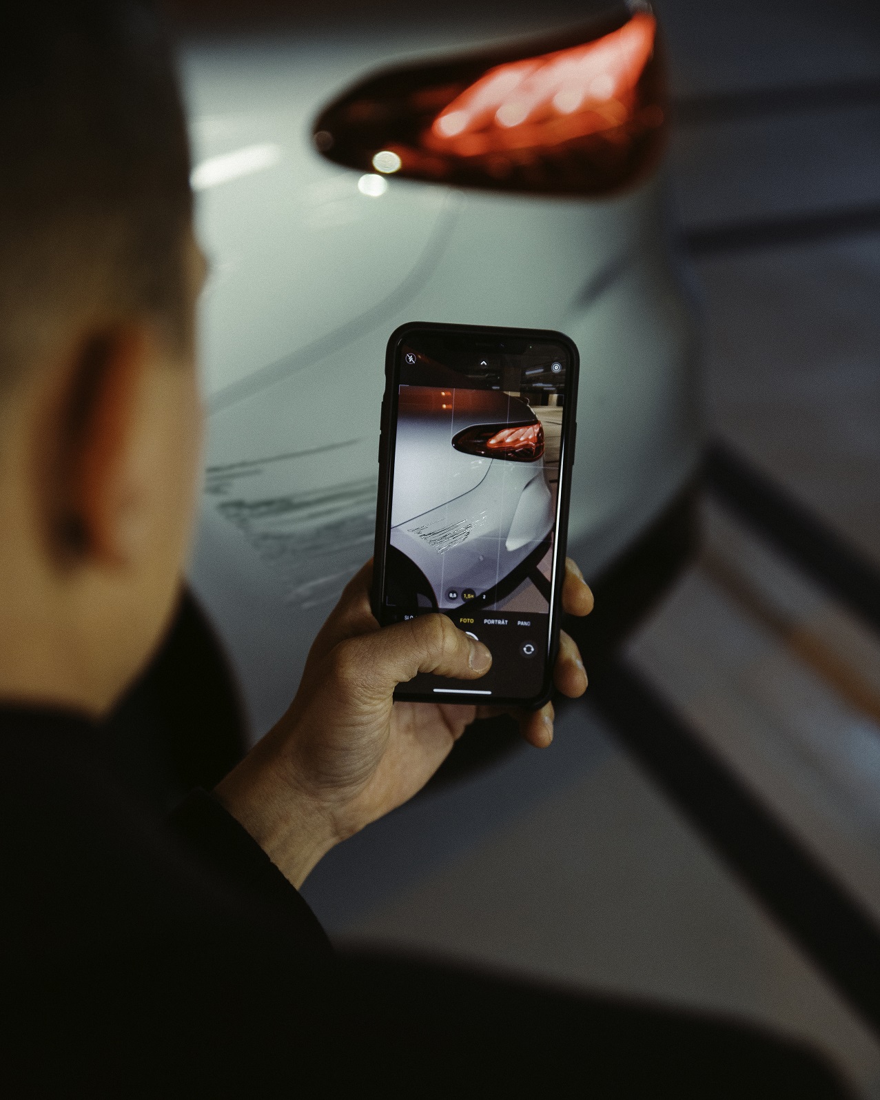 Hulp bij schade | Mercedes-Benz Een man fotografeert met een smartphone de schade aan het achterste spatscherm van zijn Mercedes-Benz.