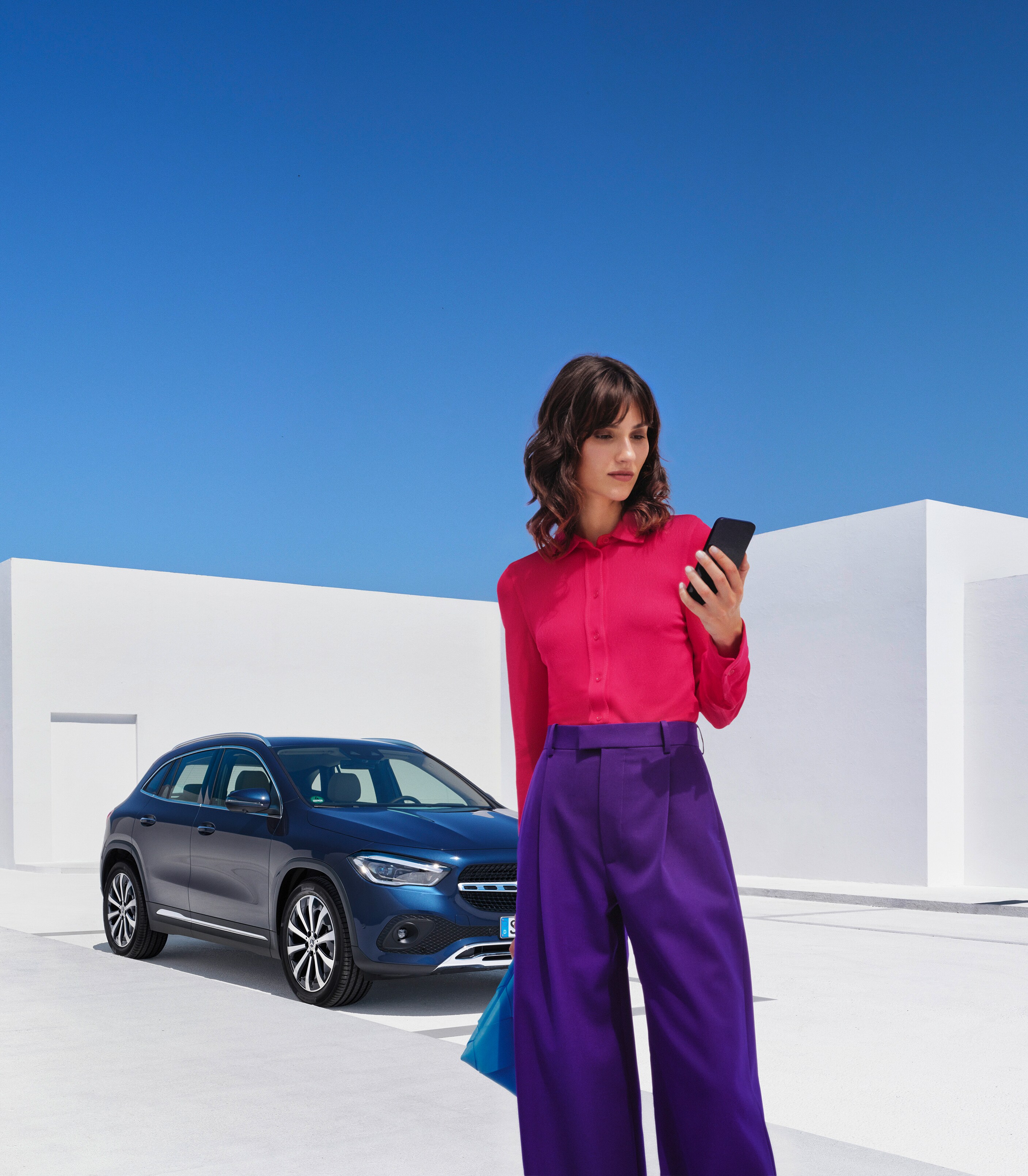 Een vrouw staat voor haar Mercedes-Benz en kijkt naar haar smartphone.
