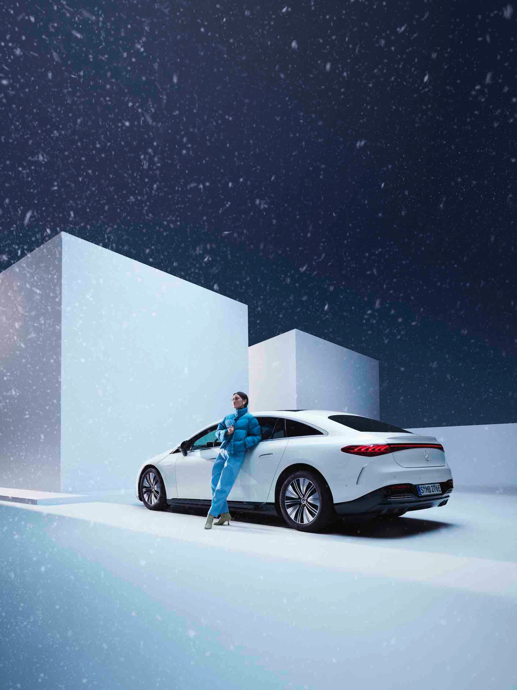 Een vrouw leunt tegen haar Mercedes-Benz aan terwijl het sneeuwt.