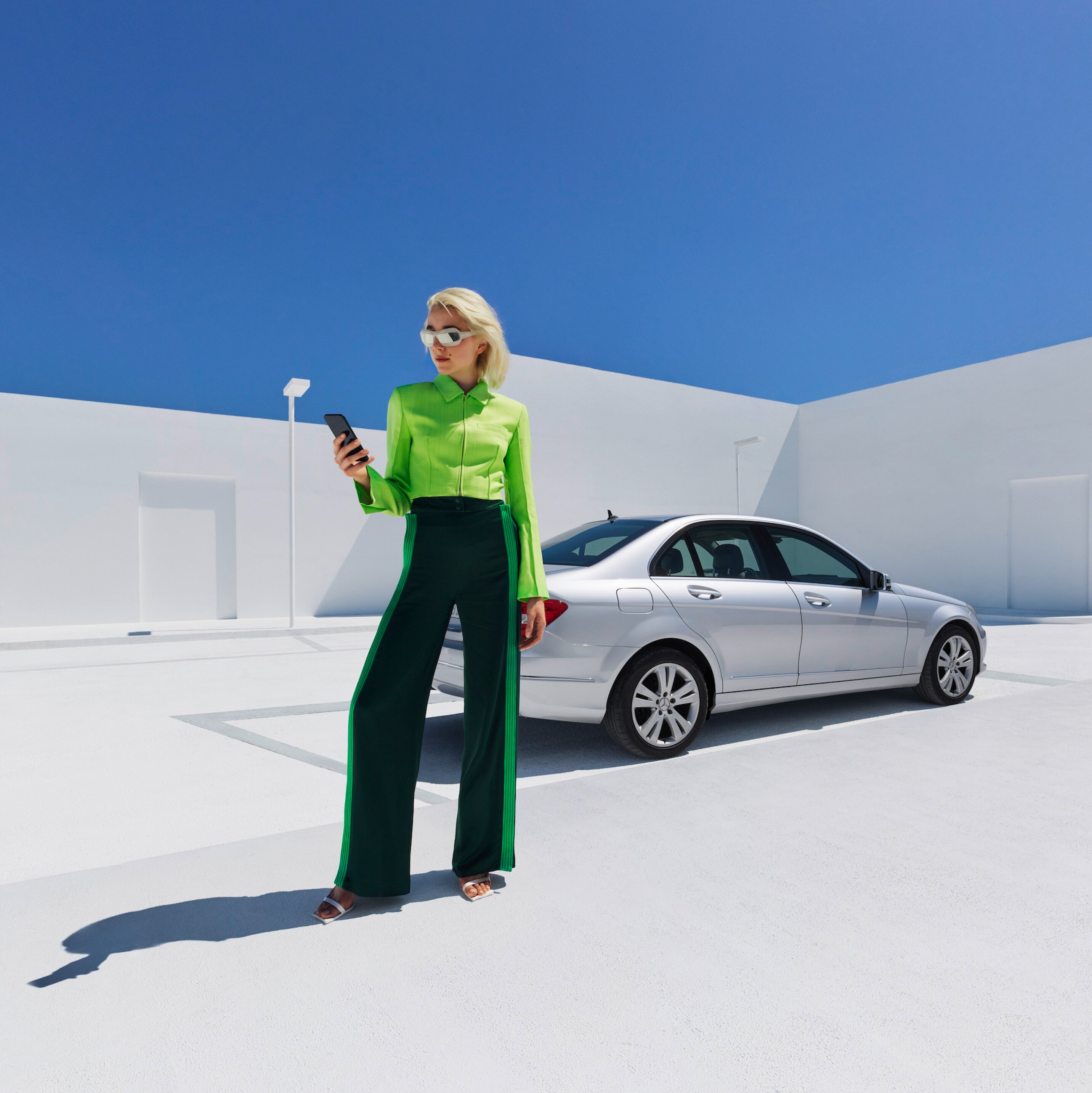 Een vrouw staat voor een Mercedes-Benz en kijkt naar haar smartphone.