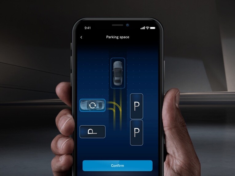 Met een smartphone wordt een Mercedes-Benz via de remote parkeerservice van de Mercedes me App ingeparkeerd.