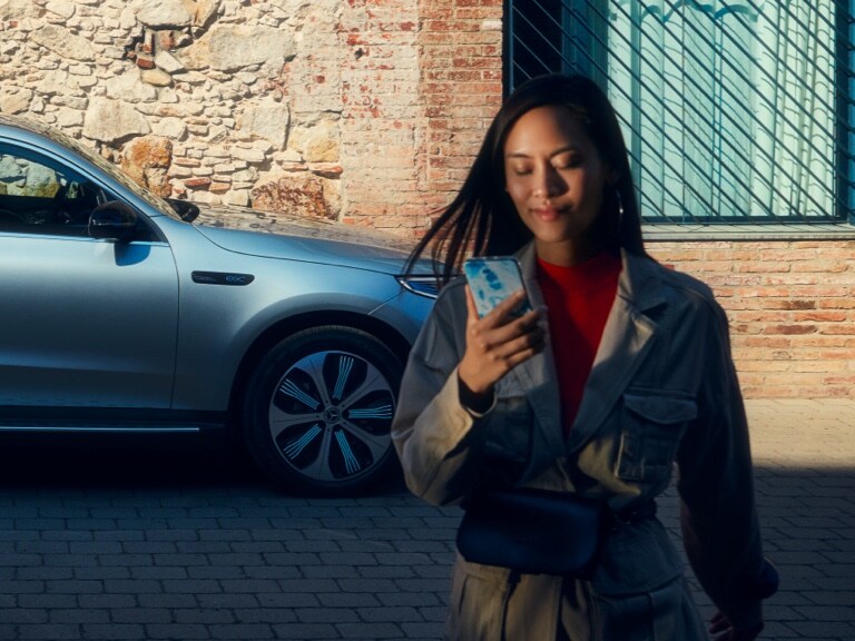 Een vrouw gebruikt de Mercedes me App op haar smartphone om een verbinding met haar Mercedes-Benz tot stand te brengen.