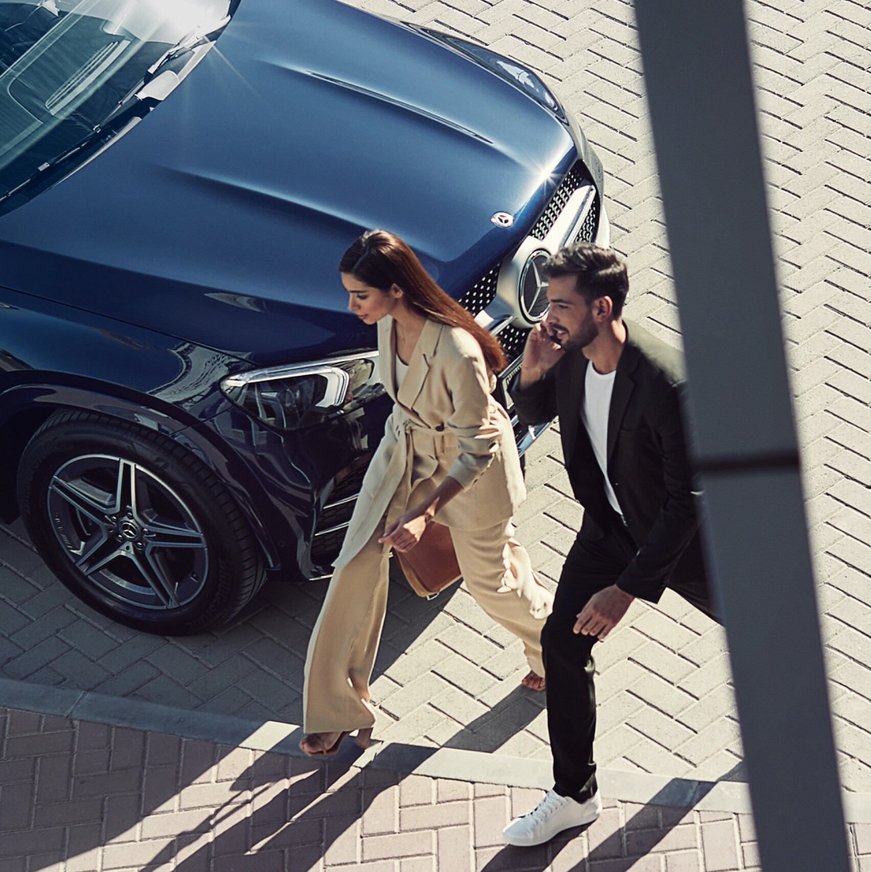Een vrouw en een man lopen langs hun Mercedes-Benz en zijn via het digitale extra met de smartphone verbonden met de auto.