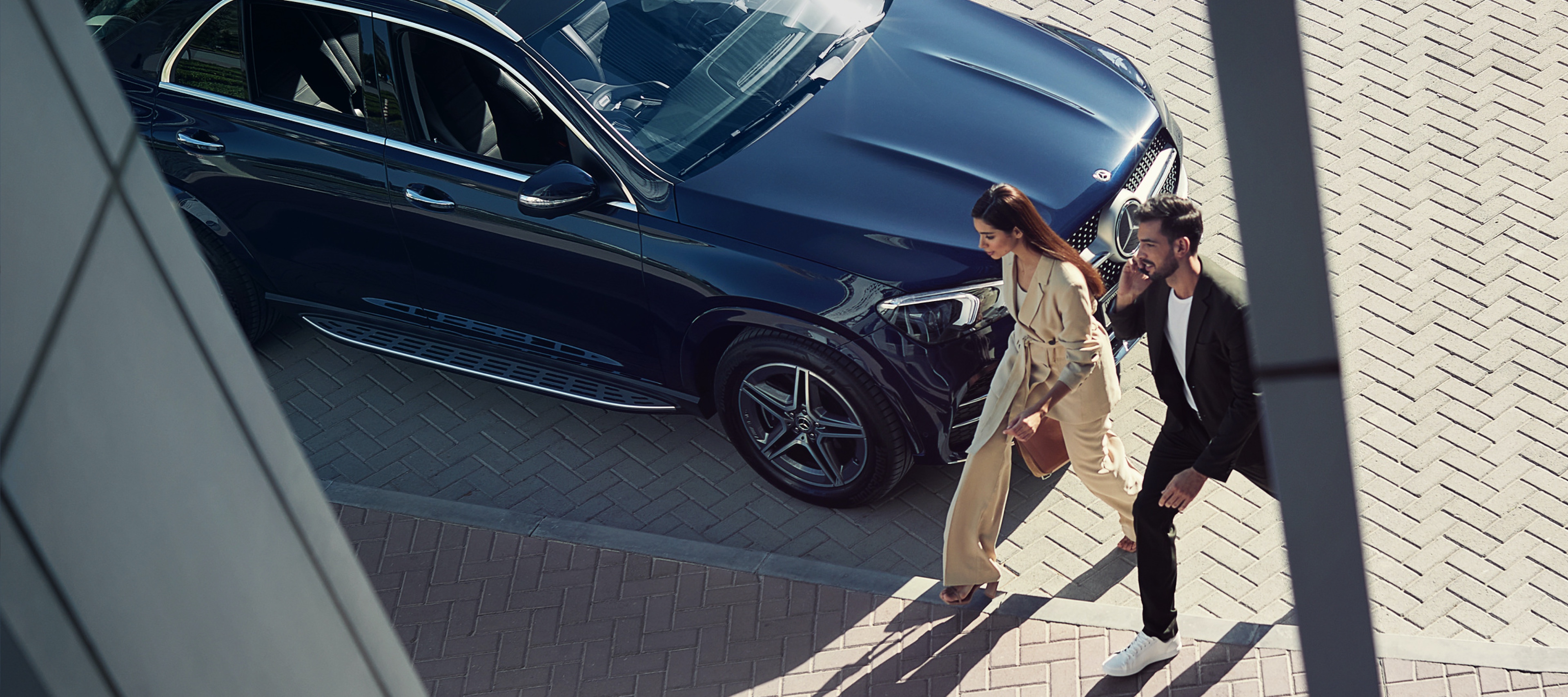 Een vrouw en een man lopen langs hun Mercedes-Benz en zijn via het digitale extra met de smartphone verbonden met de auto. Een vrouw en een man lopen langs hun Mercedes-Benz en zijn via het digitale extra met de smartphone verbonden met de auto.