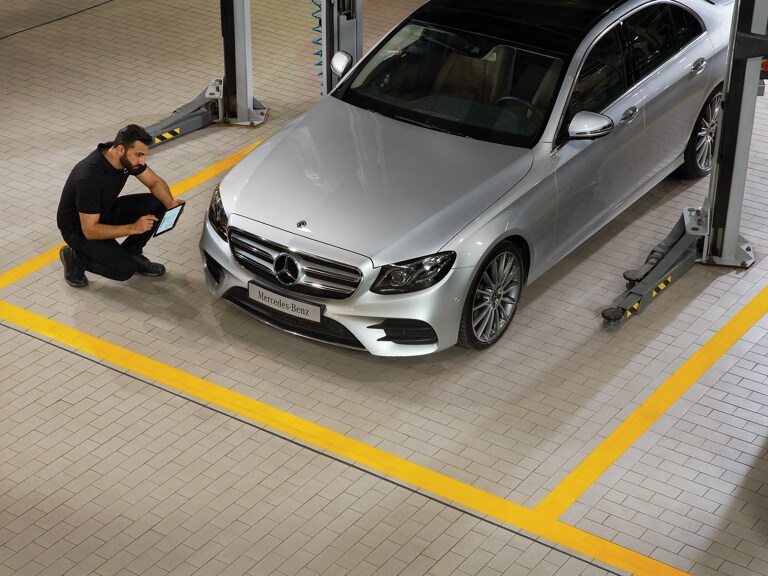 Een Mercedes-Benz technicus knielt voor een auto en voert de periodieke keuring uit.