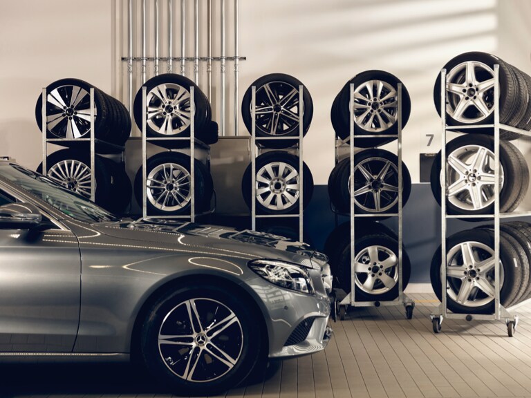Een Mercedes-Benz staat voor enkele rekken met opgeslagen banden.