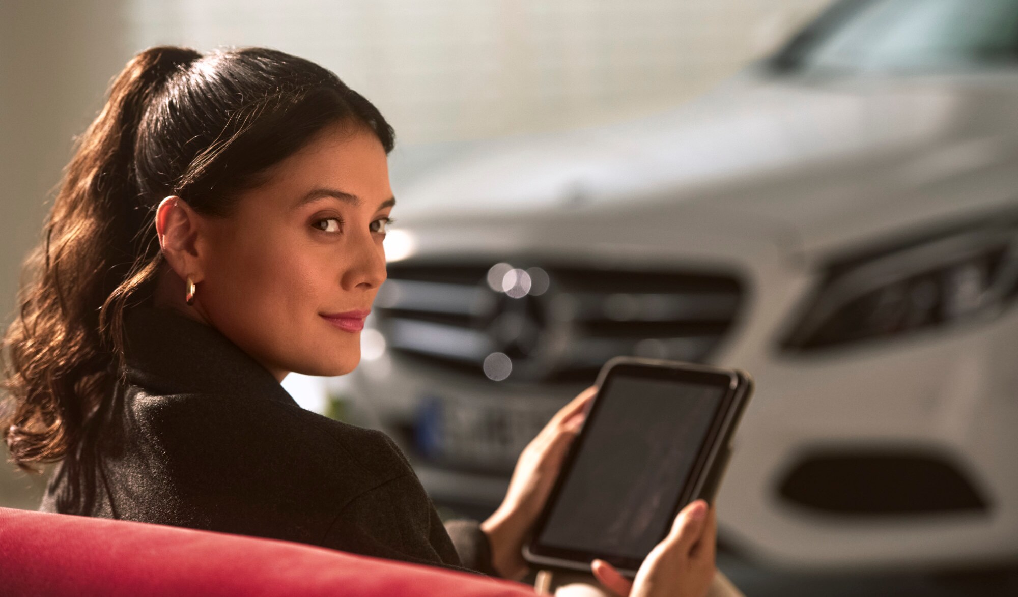 Een persoon die naast een Mercedes-Benz voertuig zit met een tablet in zijn handen.