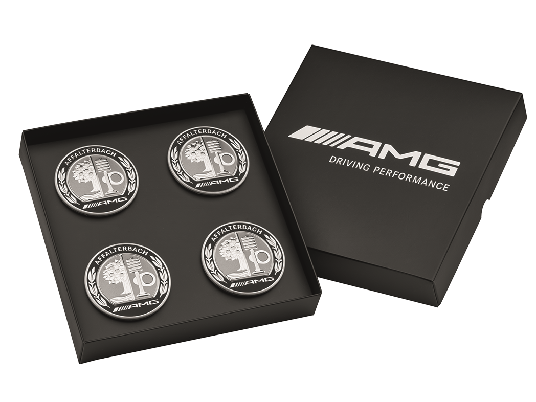 Vier zilverkleurig-zwarte AMG-naafdoppen met logo liggen in een zwarte box.
