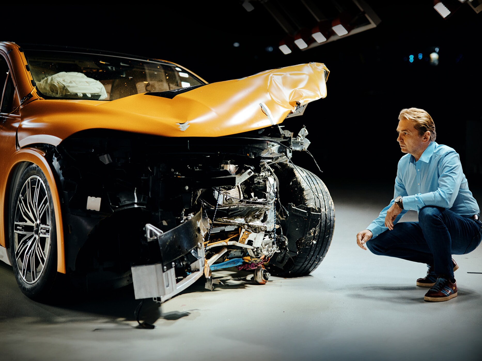 Crashtestexpert inspecteert een frontaal beschadigde Mercedes-Benz terwijl hij ernaast gehurkt zit.