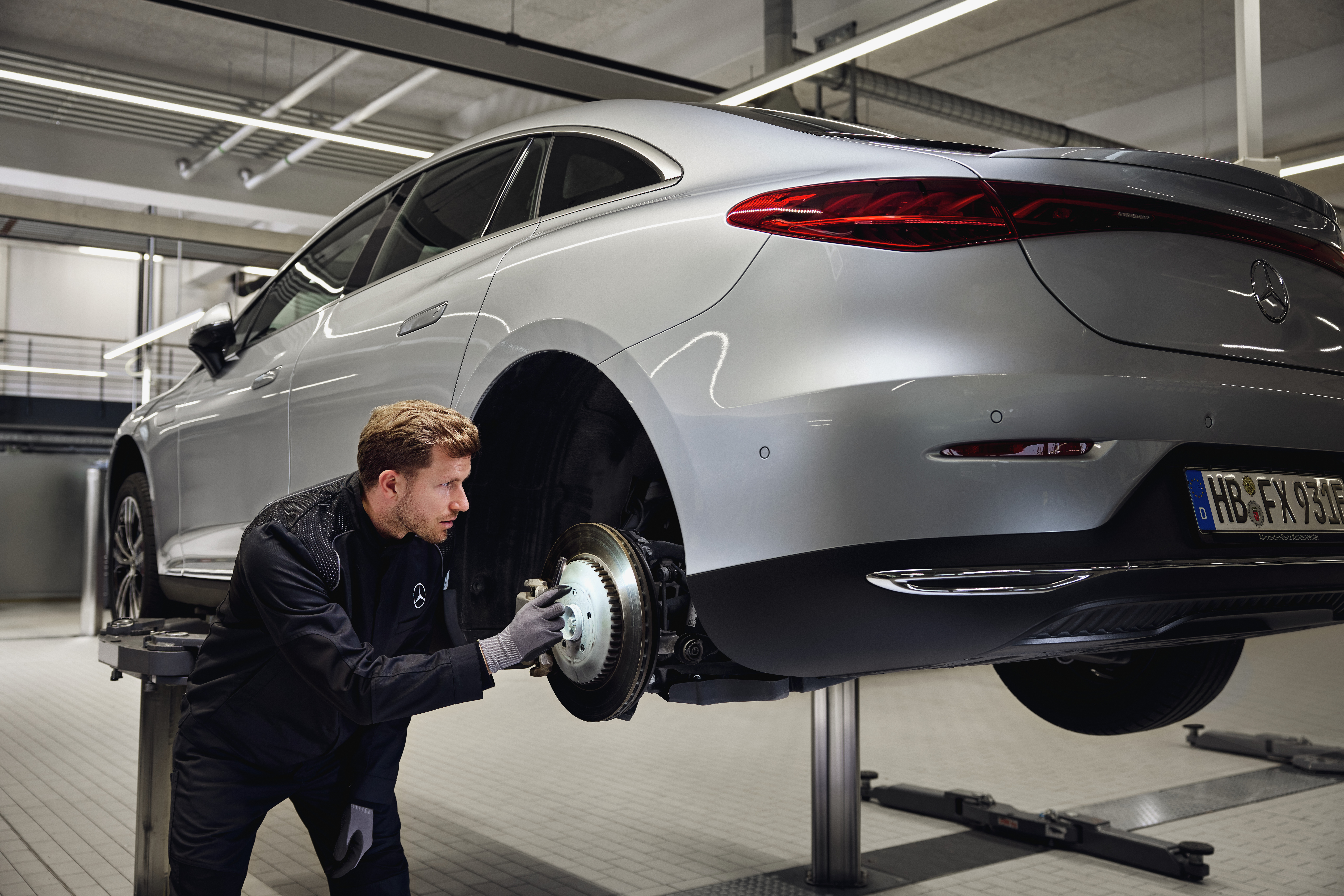 Mercedes-Benz originele remvervanging Mercedes-Benz voertuig omhoog op een lift met een technicus die het achterremsysteem inspecteert voor een vervanging van originele onderdelen service.
