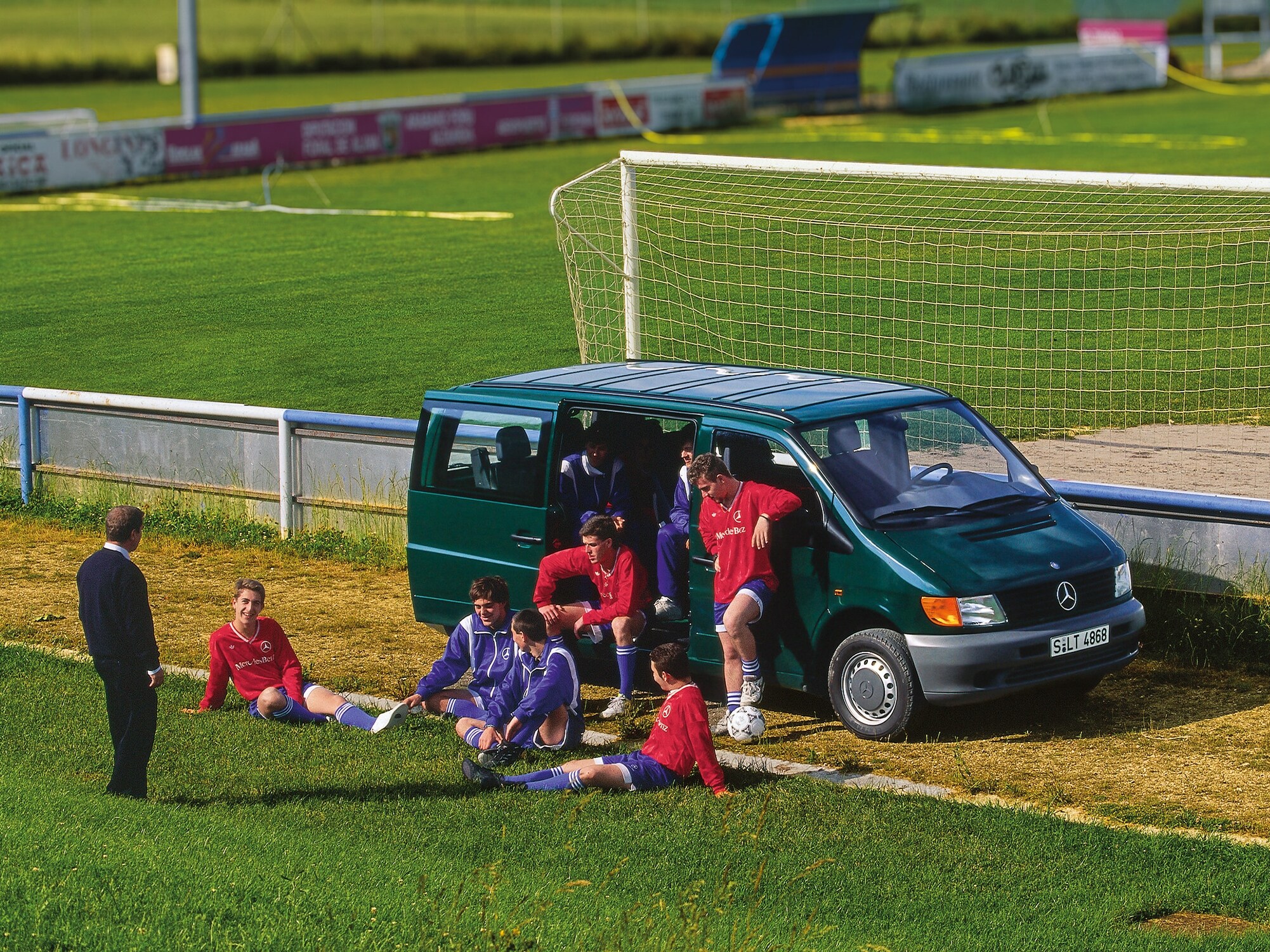 Een Vito van de eerste generatie staat geparkeerd naast een voetbalveld, met spelers van het team in de buurt