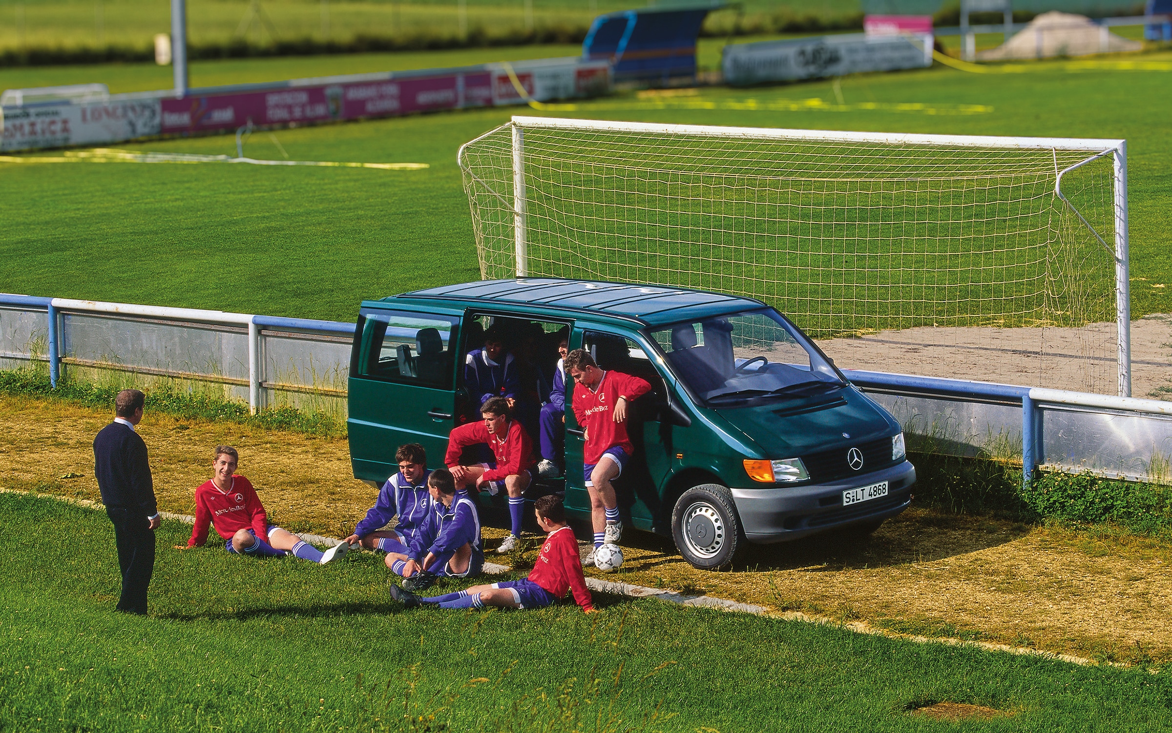 De eerste generatie Mercedes-Benz Vito’s | Geschiedenis van bedrijfswagens | Mercedes-Benz Een Vito van de eerste generatie staat geparkeerd naast een voetbalveld, met spelers van het team in de buurt