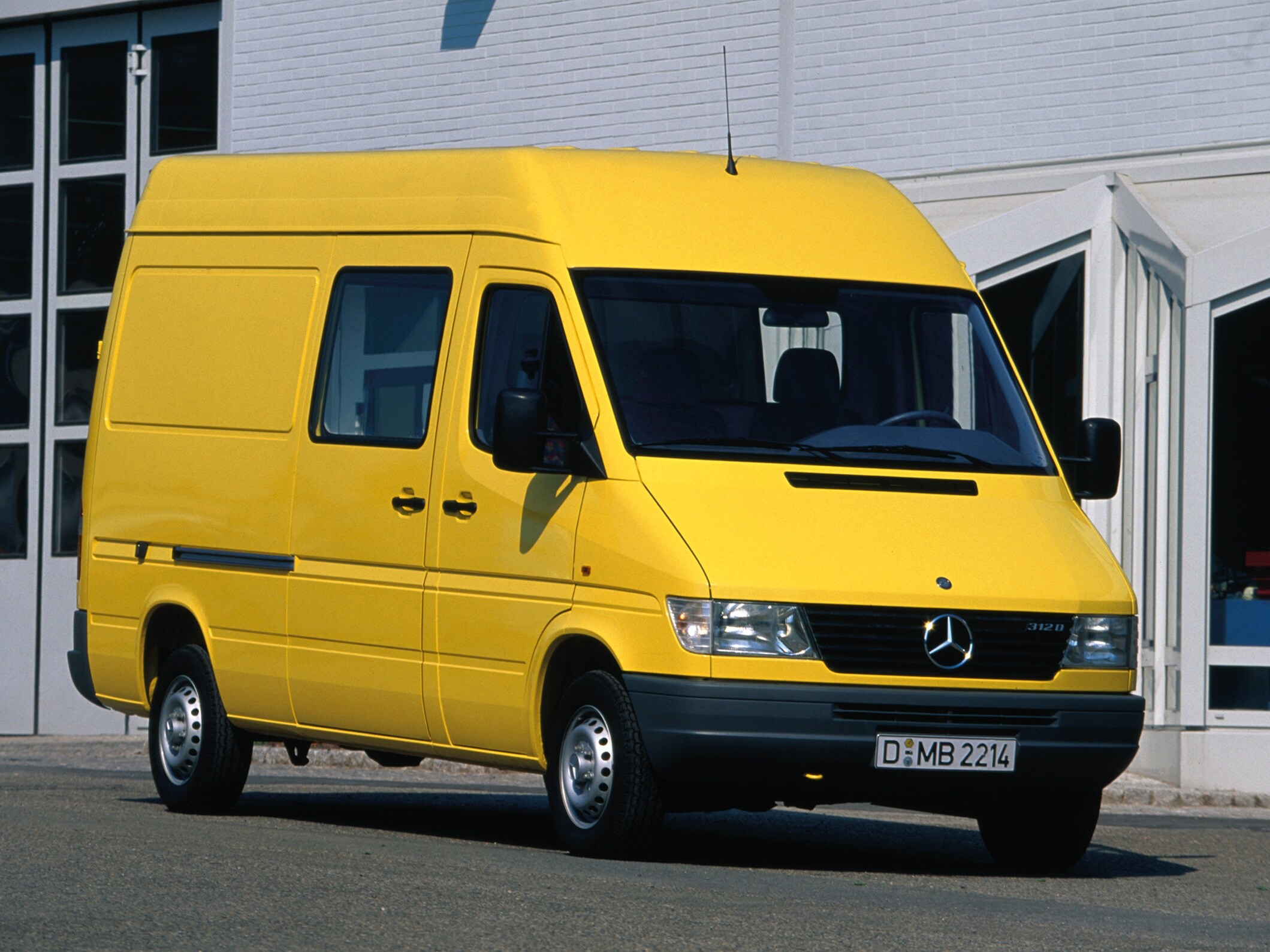 Een Sprinter van de eerste generatie staat geparkeerd voor een bedrijfsgebouw