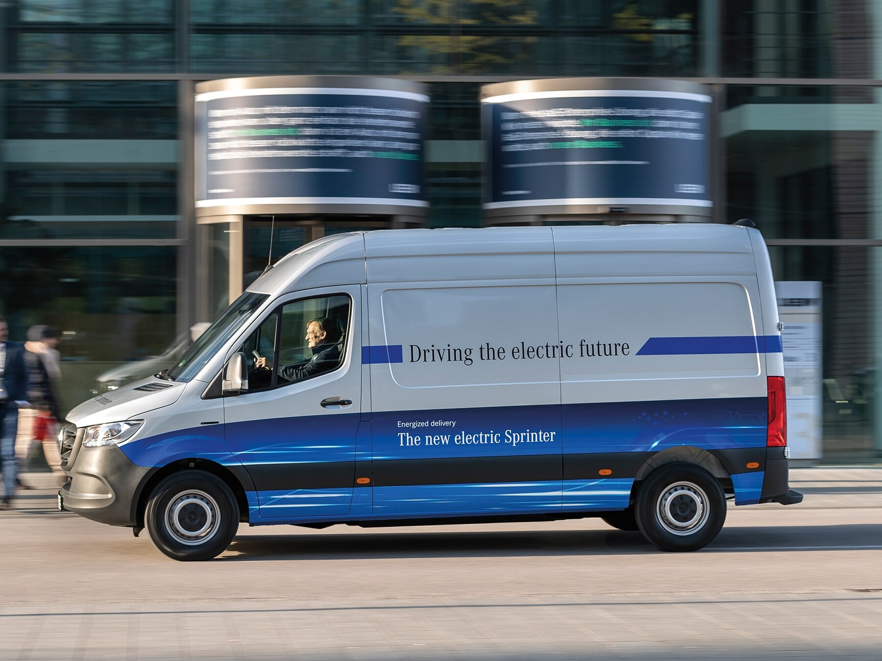 Een Mercedes-Benz eSprinter bestelwagen rijdt door een moderne stadsstraat