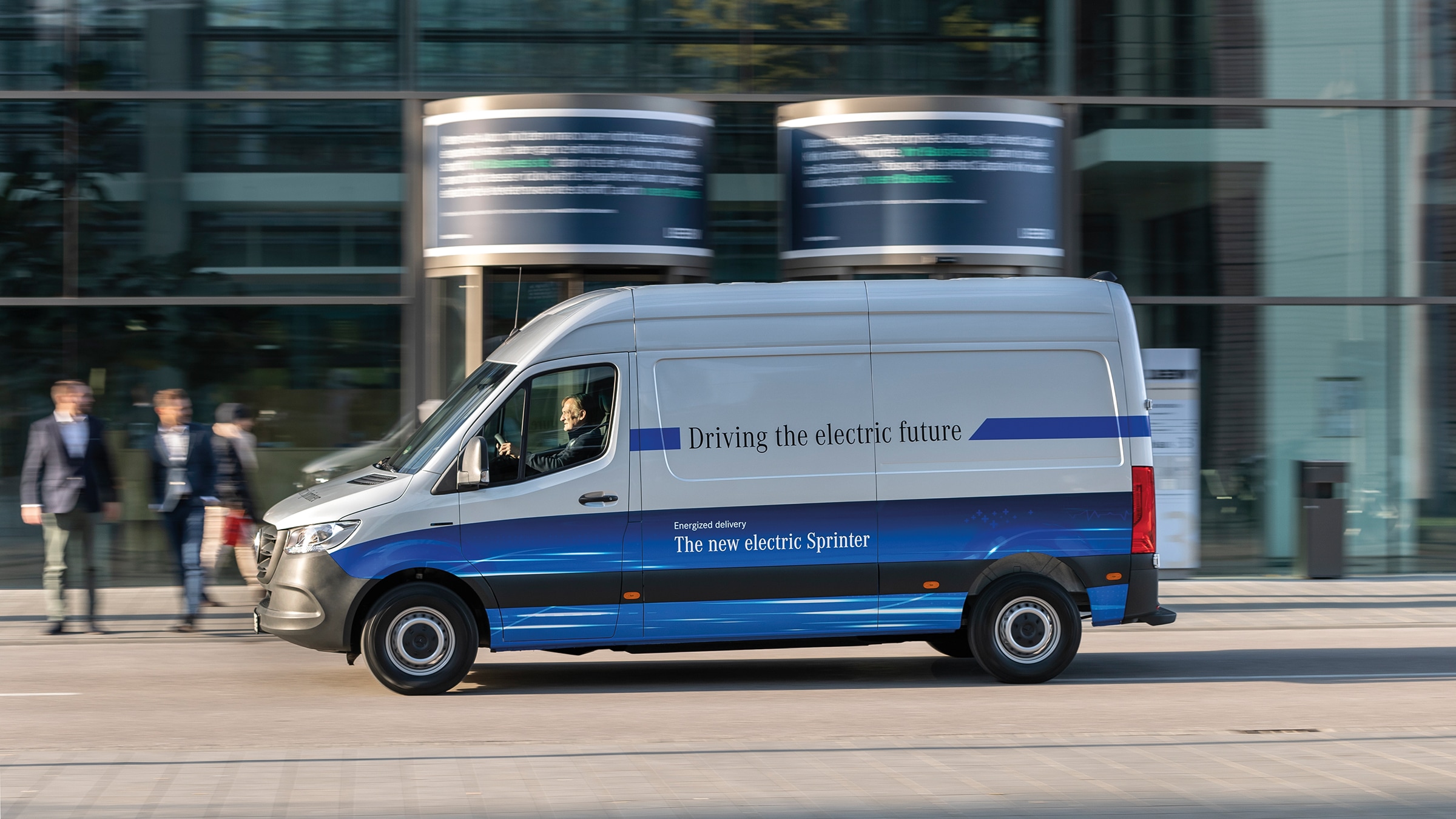 De eSprinter gesloten bestelwagen van de tweede generatie | Geschiedenis van bedrijfswagens | Mercedes-Benz Een Mercedes-Benz eSprinter bestelwagen rijdt door een moderne stadsstraat