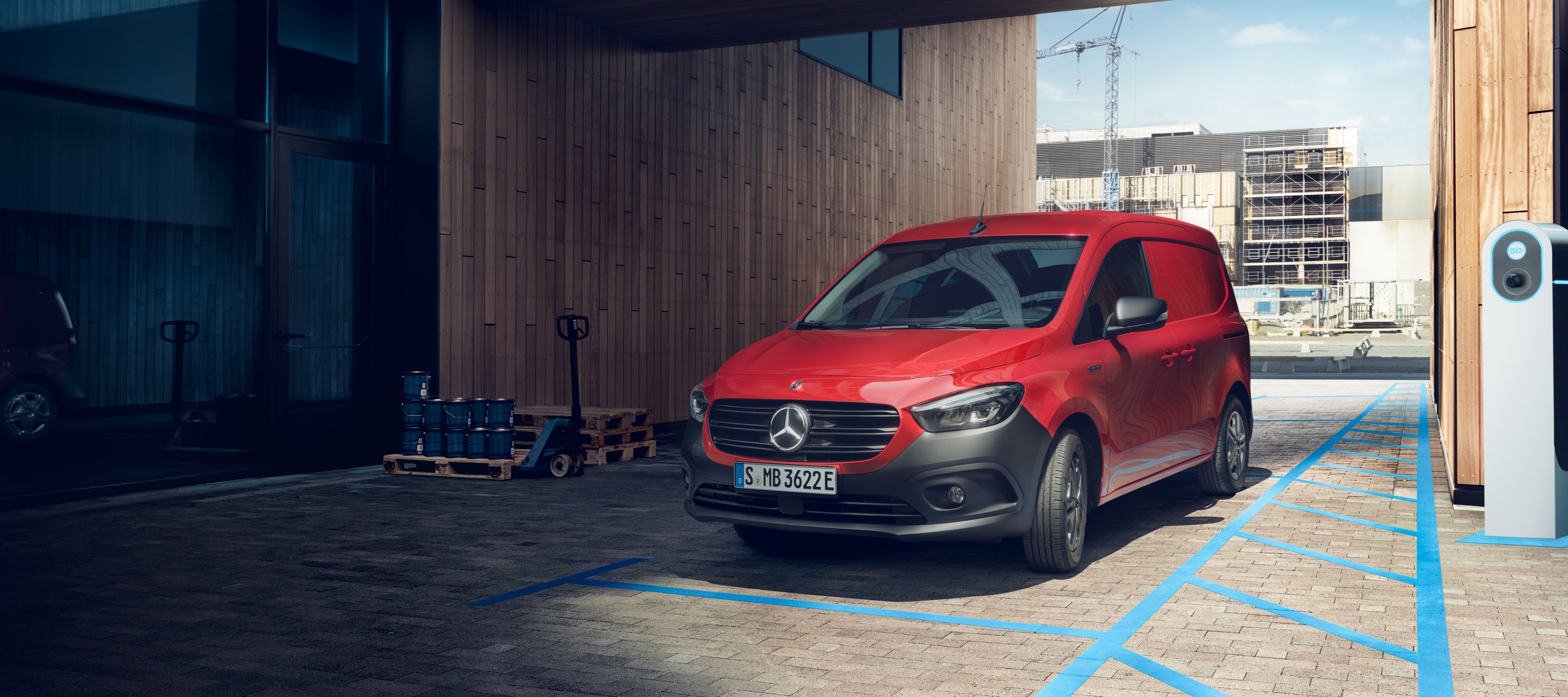 eCitan Gesloten Bestelwagen | Mercedes-Benz Bestelwagens De eCitan Gesloten Bestelwagen, een elektrische bestelwagen van Mercedes-Benz, parkeert bij een laadpunt voor een modern gebouw.