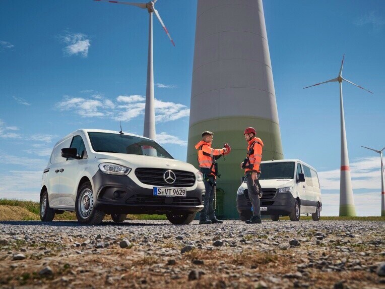 Twee Mercedes-Benz bestelwagens en twee mensen in opvallende kleding voor een windmolenpark.