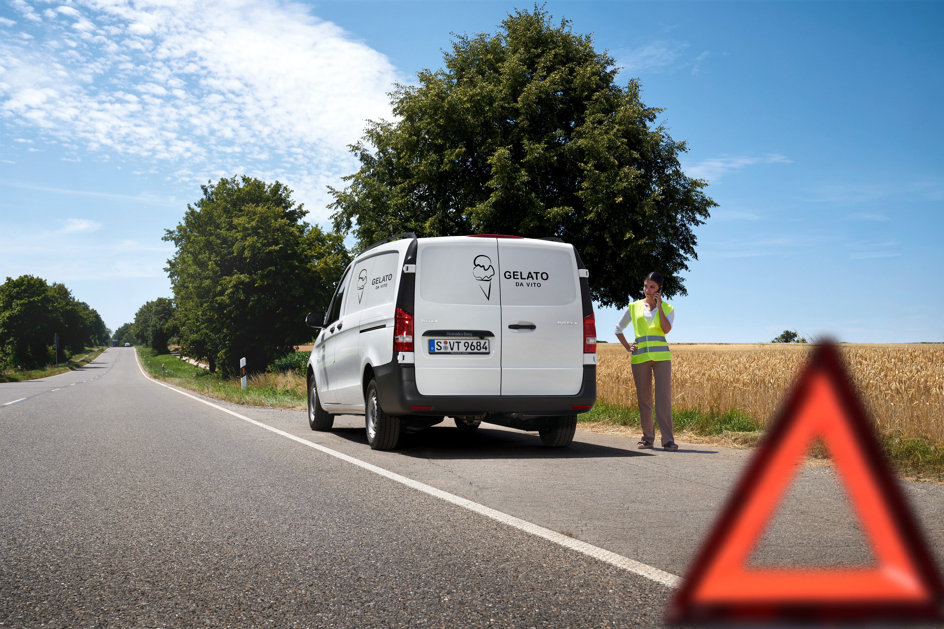 Mercedes-Benz | Van Care | Service24h Een vrouw belt de Mercedes-Benz Service24h-hotline, terwijl een Mercedes-Benz Sprinter langs een landweg stilstaat.