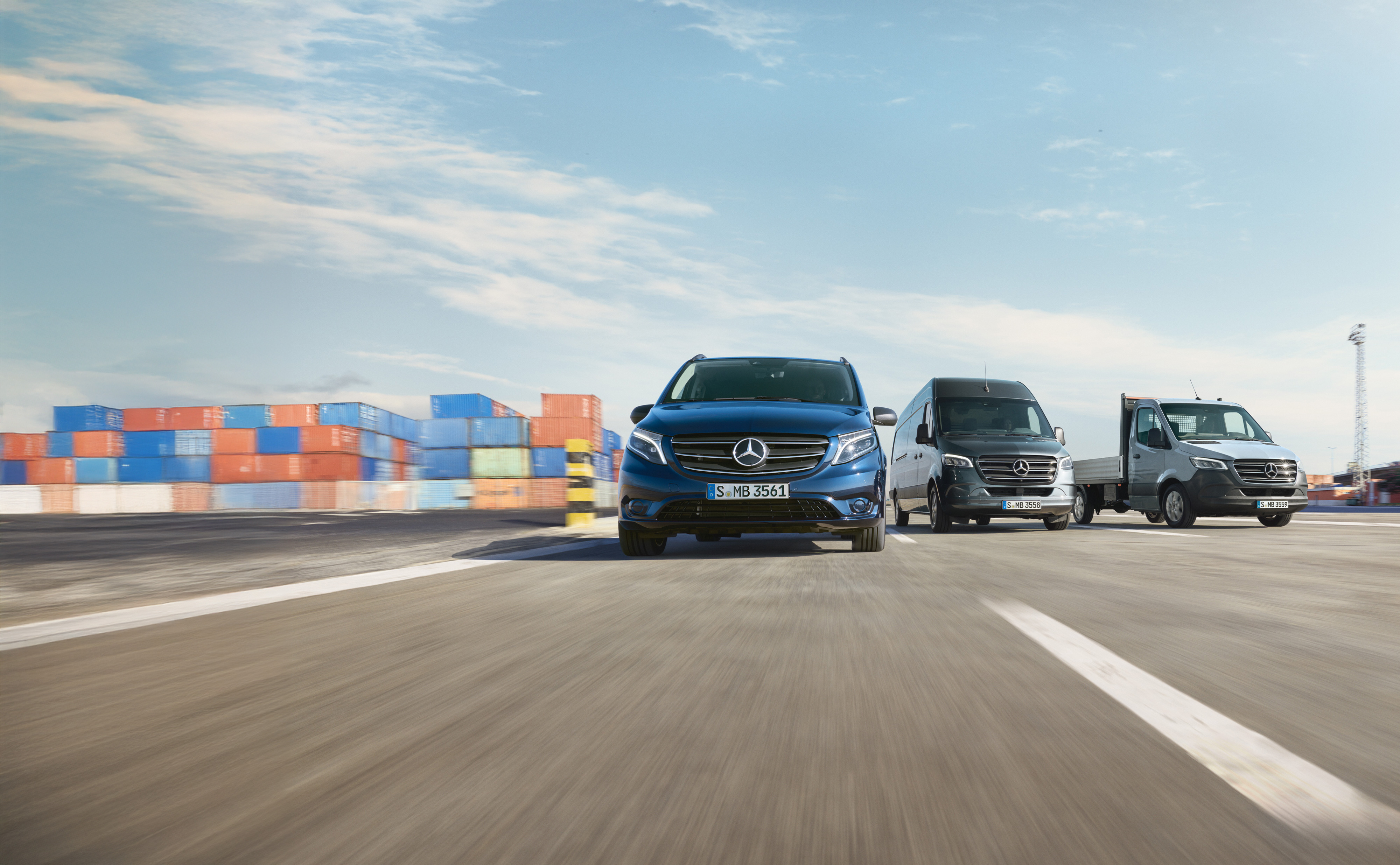 Mercedes-Benz | Van Care | Service24h Een reeks Mercedes-Benz bestelwagens die naast elkaar geparkeerd staan op een weg naast een laadkade.