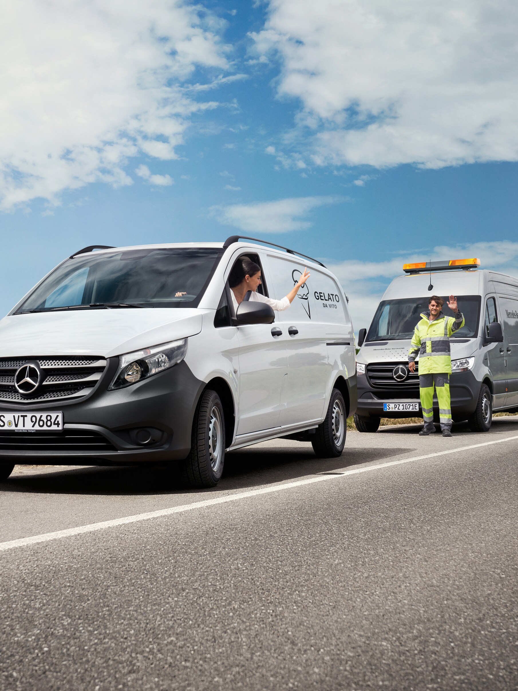 Een persoon in een witte Mercedes-Benz Vito die zwaait naar een servicemonteur die langs de weg geparkeerd staat.