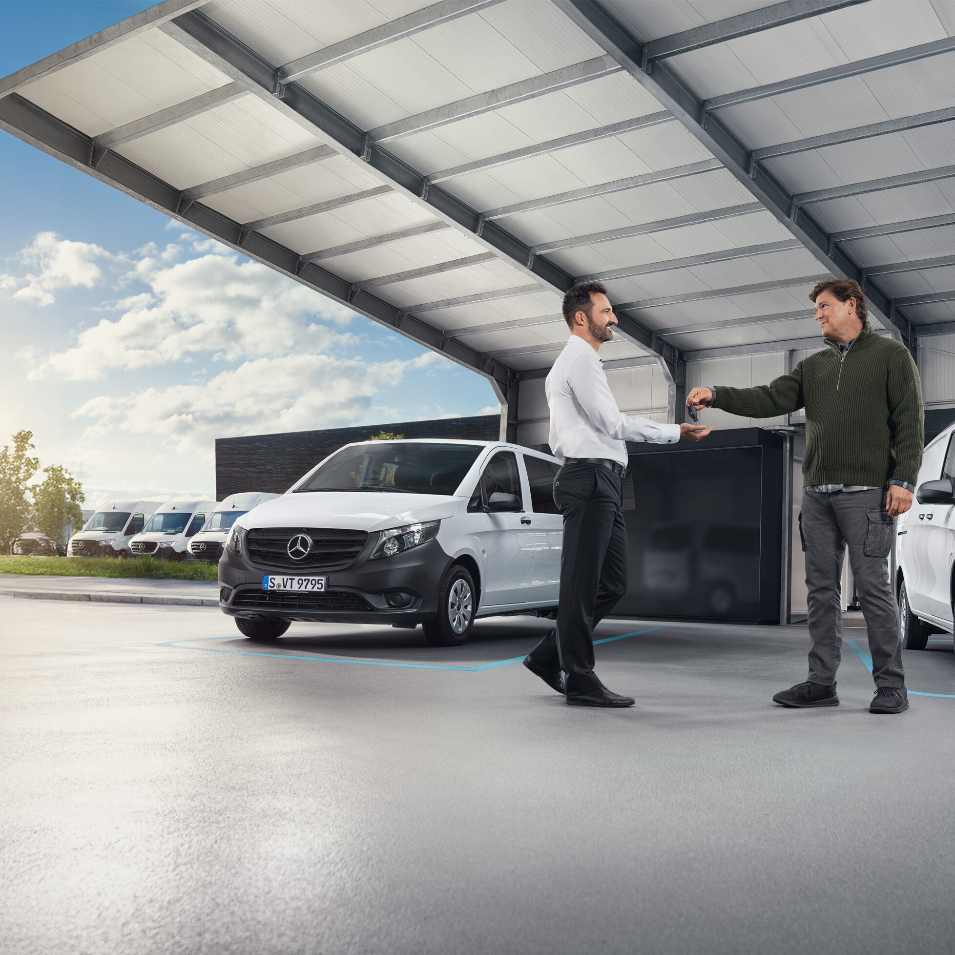 Twee mannen in gesprek voor een reeks witte Mercedes-Benz bestelwagens in een hal