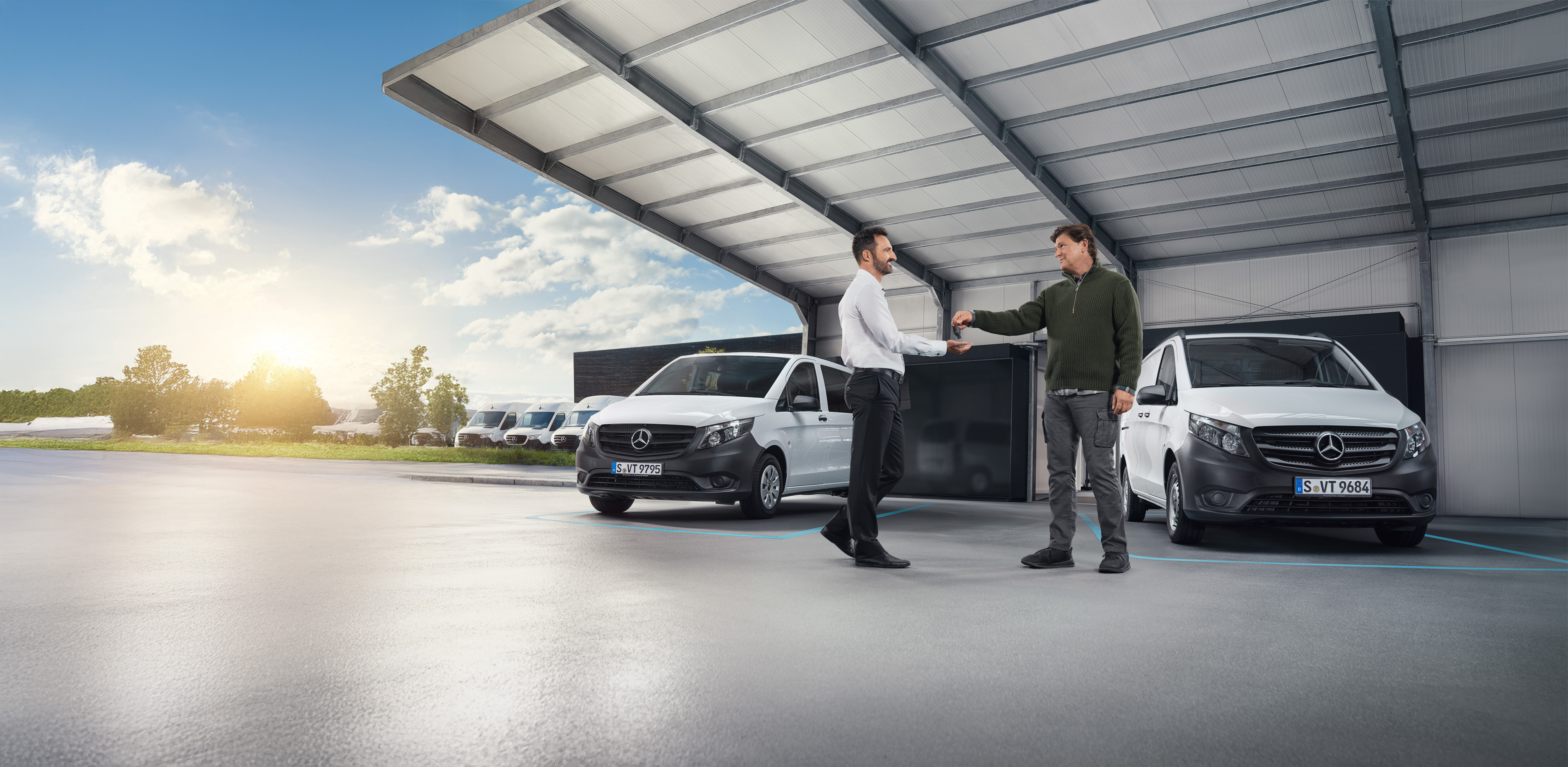 Mercedes-Benz | Van Care | Individuele ondersteuning Twee mannen in gesprek voor een reeks witte Mercedes-Benz bestelwagens in een hal