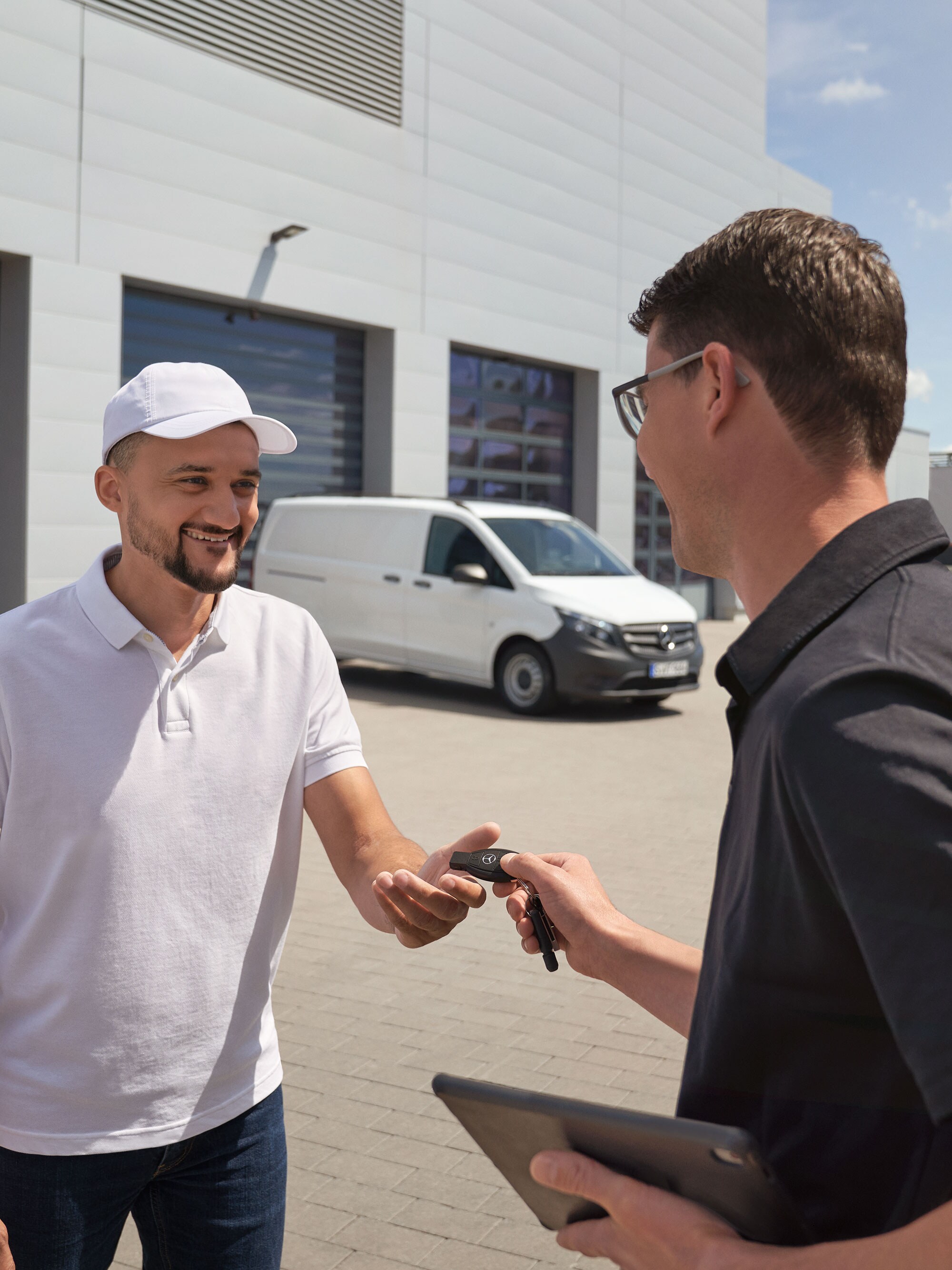Mercedes-Benz technicus overhandigt sleutels aan een klant met een witte Mercedes-Benz Vito bestelwagen op de achtergrond.
