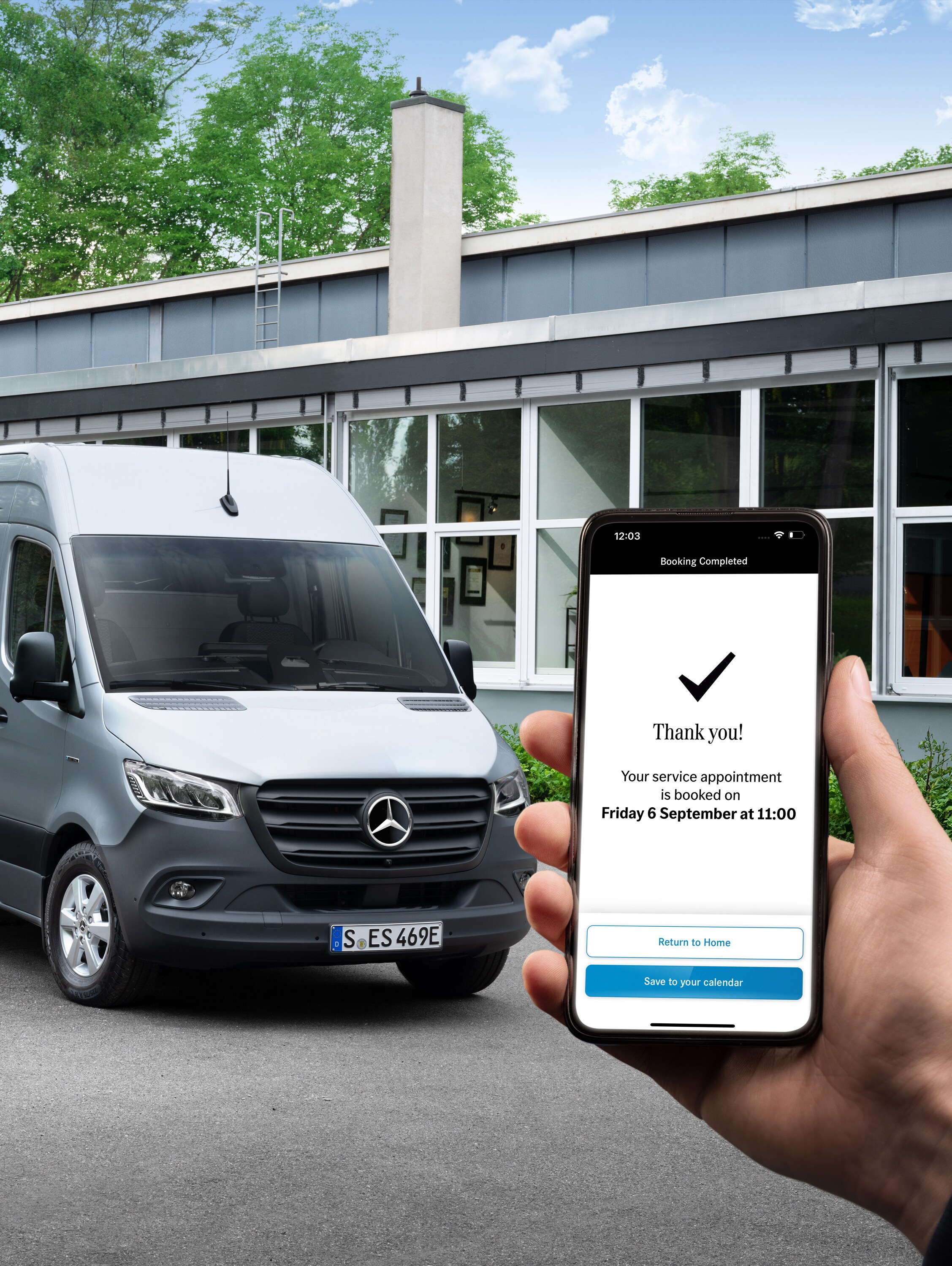 Een grijze Mercedes-Benz Sprinter bestelwagen voor een kantoor, met op de voorgrond een persoon die een smartphone vasthoudt.