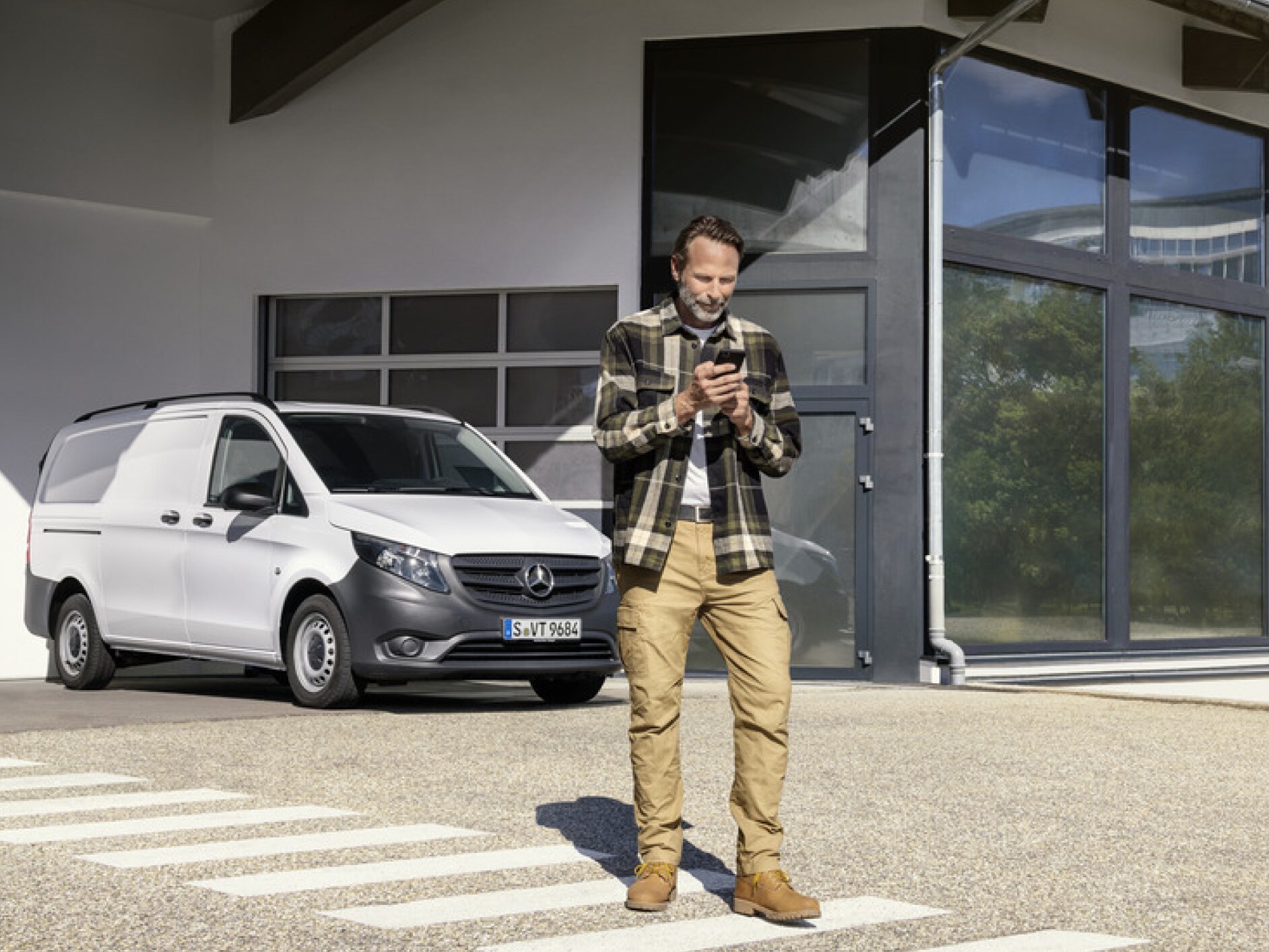 Een persoon met een smartphone voor een Mercedes-Benz Vito.