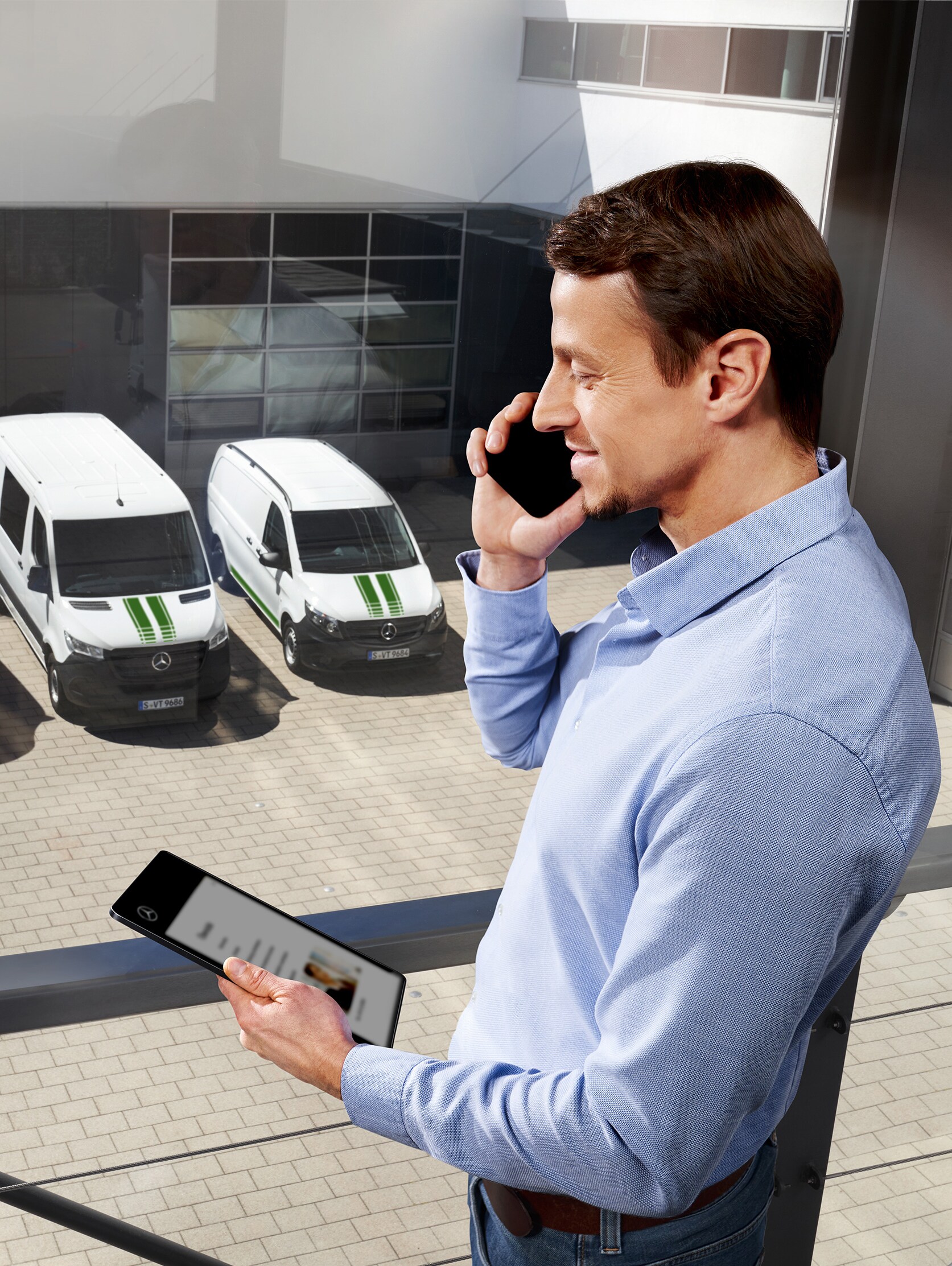 Man aan de telefoon met tablet voor drie Mercedes-Benz busjes, onderwerp: hoe lang is de fabrieksgarantie bij Mercedes-Benz?