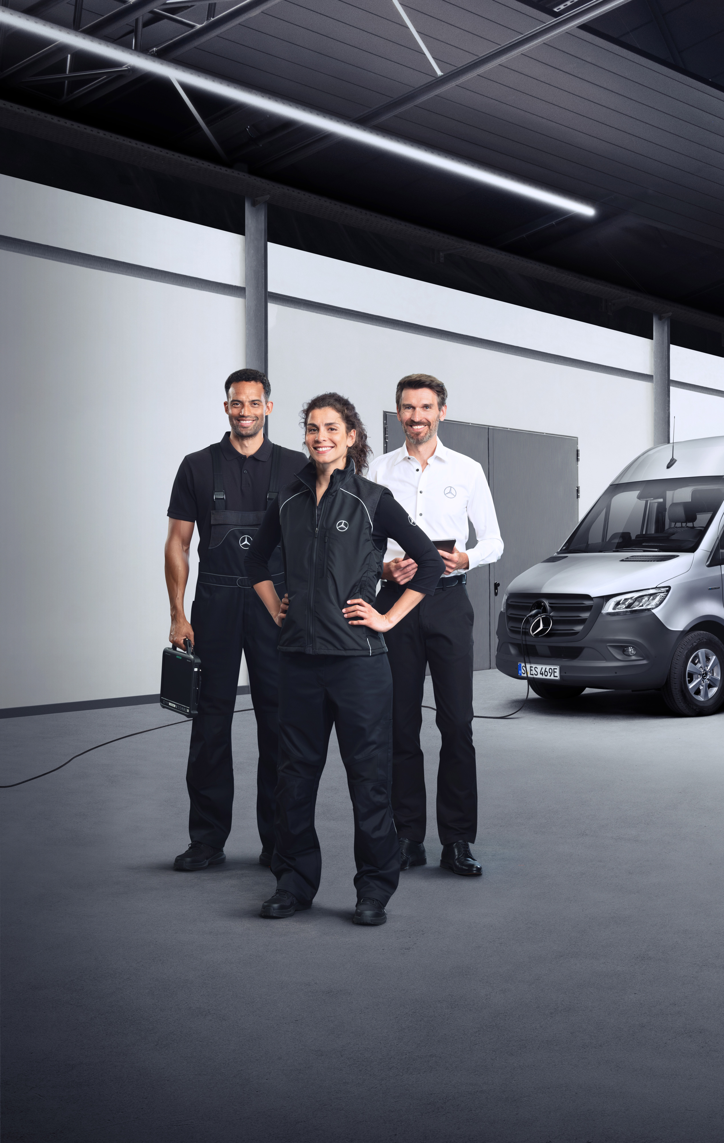 Mercedes-Benz | Servicesoverzicht | Services elektrische bestelwagens Drie medewerkers die voor een zilveren Mercedes-Benz eSprinter staan met aangesloten laadkabel.
