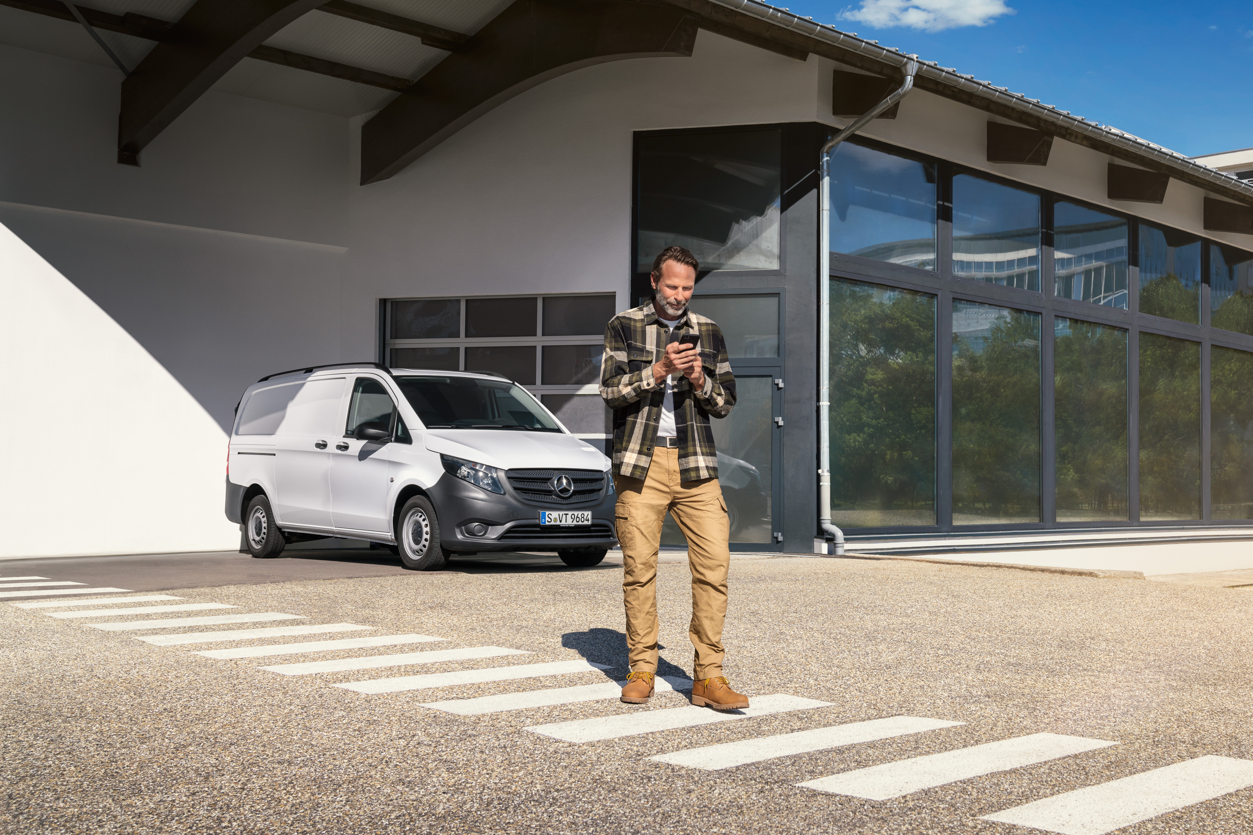 Mercedes-Benz | Service voor elektrische voertuigen | Digitale ondersteuning Een man die voor een witte Mercedes-Benz Vito Gesloten Bestelwagen staat en zijn smartphone gebruikt.
