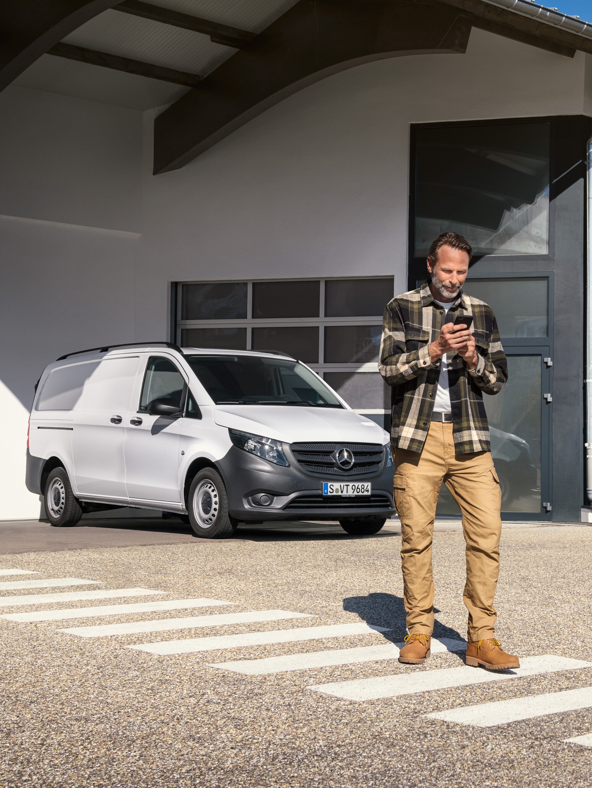Een man die voor een witte Mercedes-Benz Vito bestelwagen staat en zijn smartphone gebruikt.