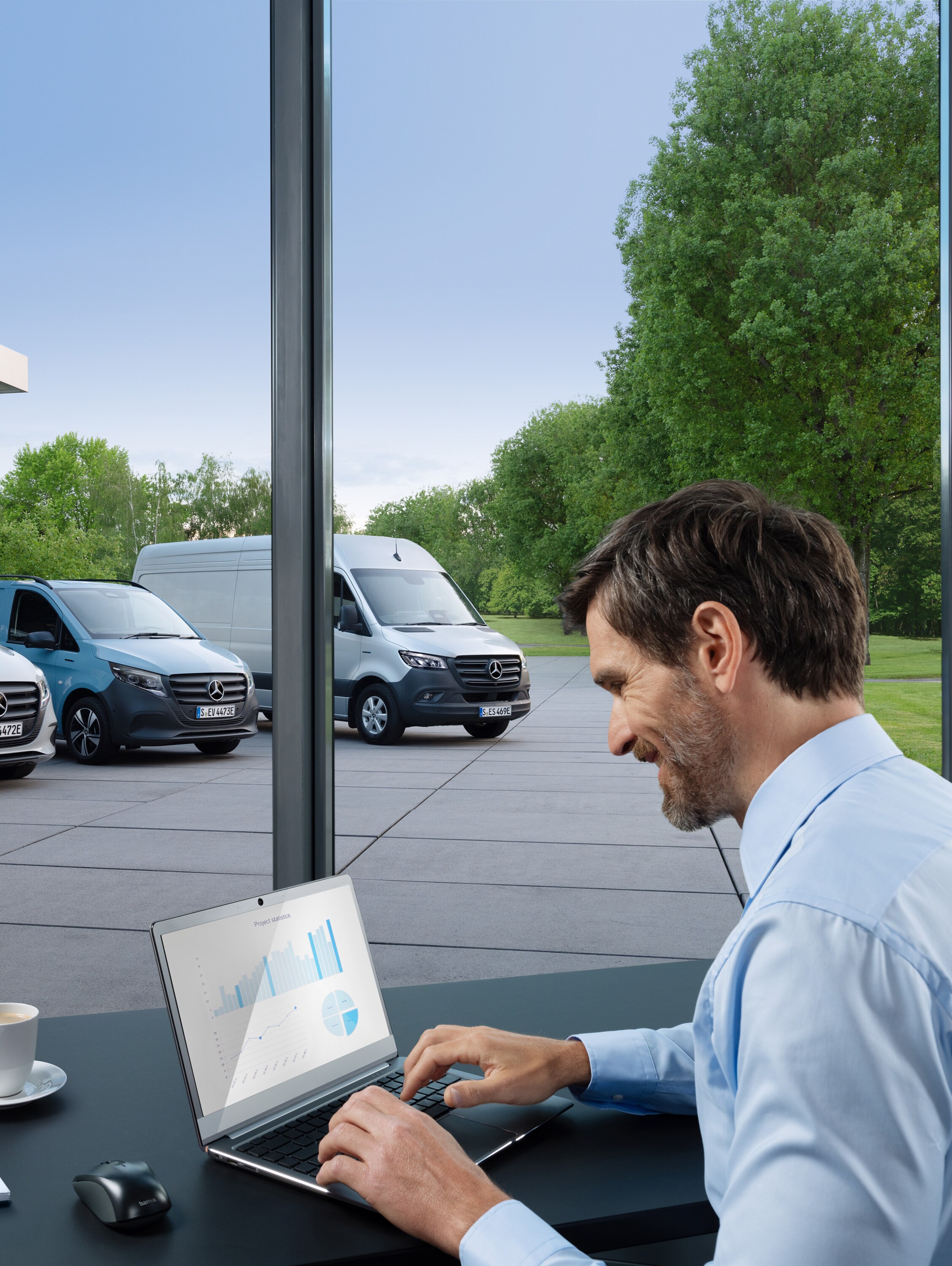 Een man die op een laptop werkt, buiten staat een reeks Mercedes-Benz bestelwagens.