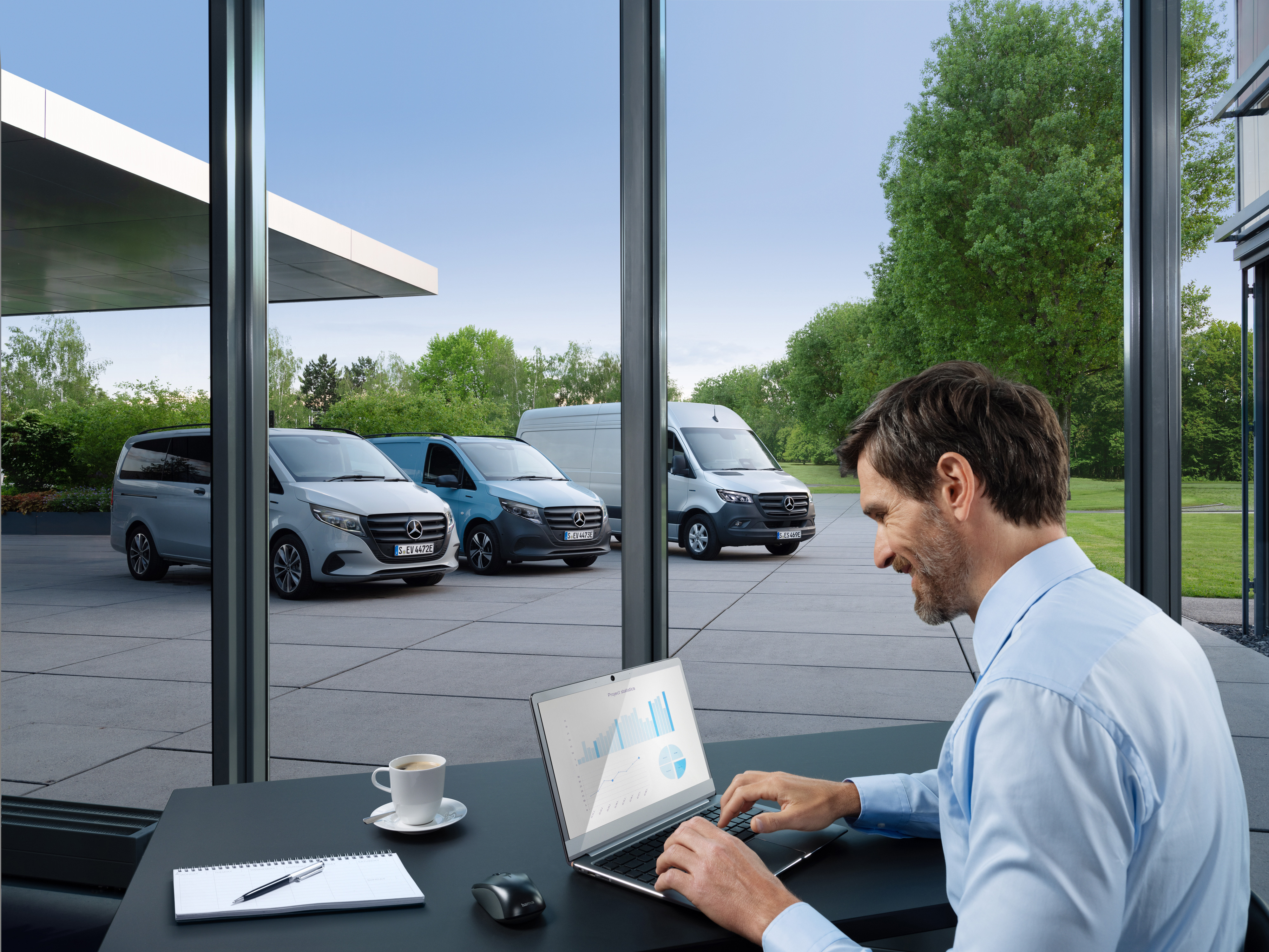 Mercedes-Benz | Service voor elektrische voertuigen | Pakketten Een man die op een laptop werkt, buiten staat een reeks Mercedes-Benz bestelwagens.