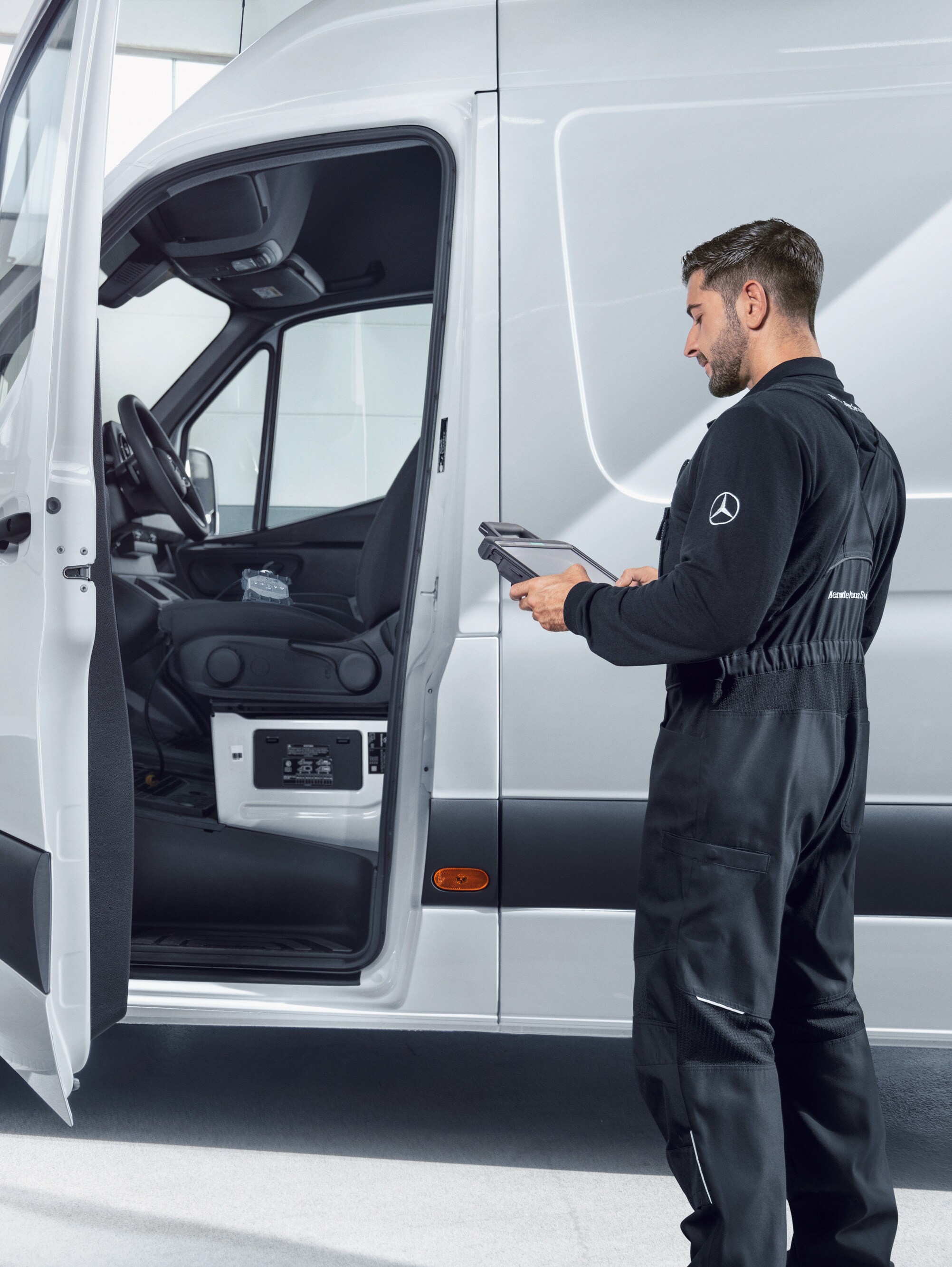 Een technicus controleert een witte Mercedes-Benz Sprinter bestelwagen met een tablet.