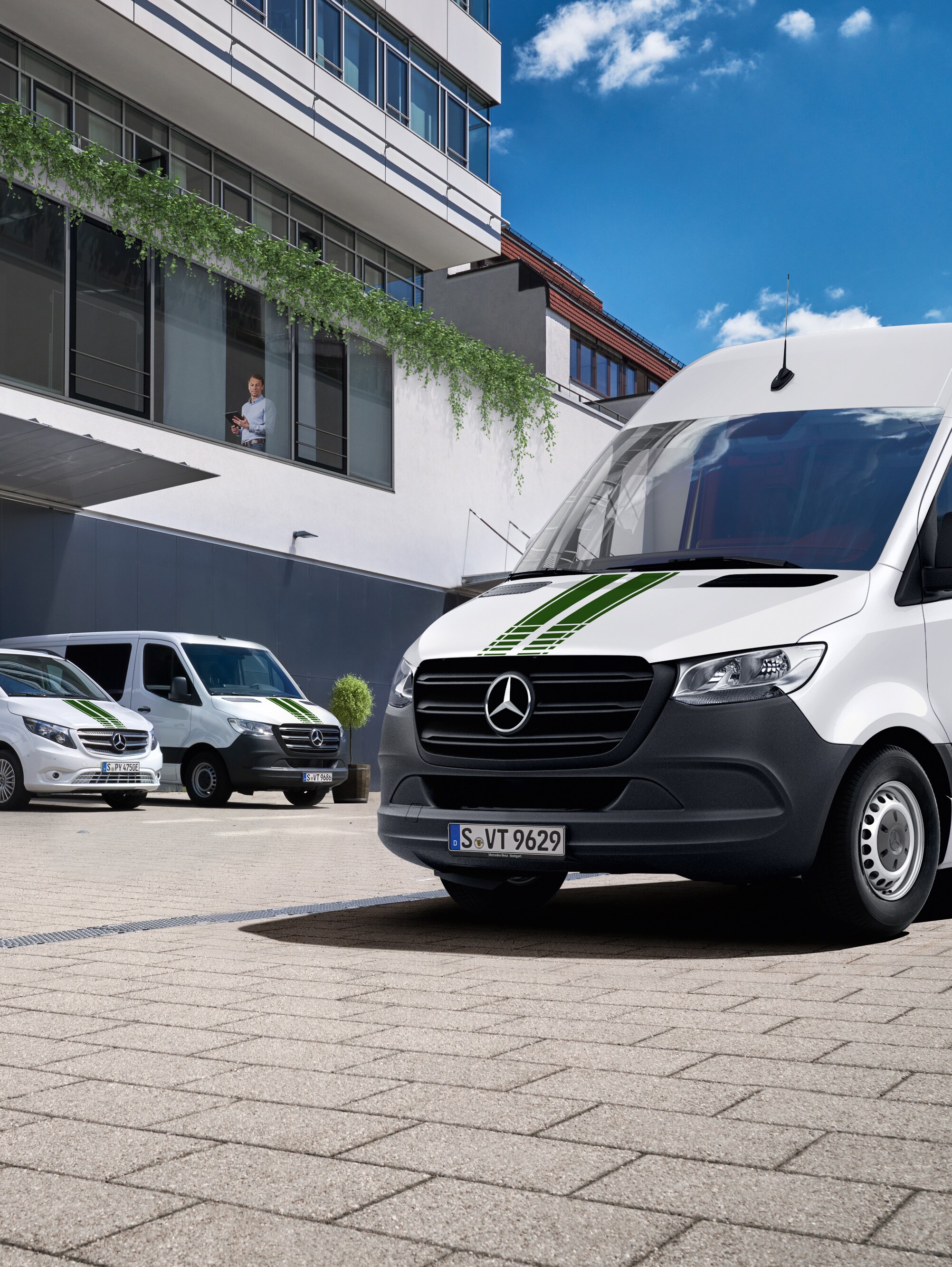 Een wagenpark witte Mercedes-Benz bestelwagens voor een kantoorgebouw op een zonnige dag met blauwe lucht.