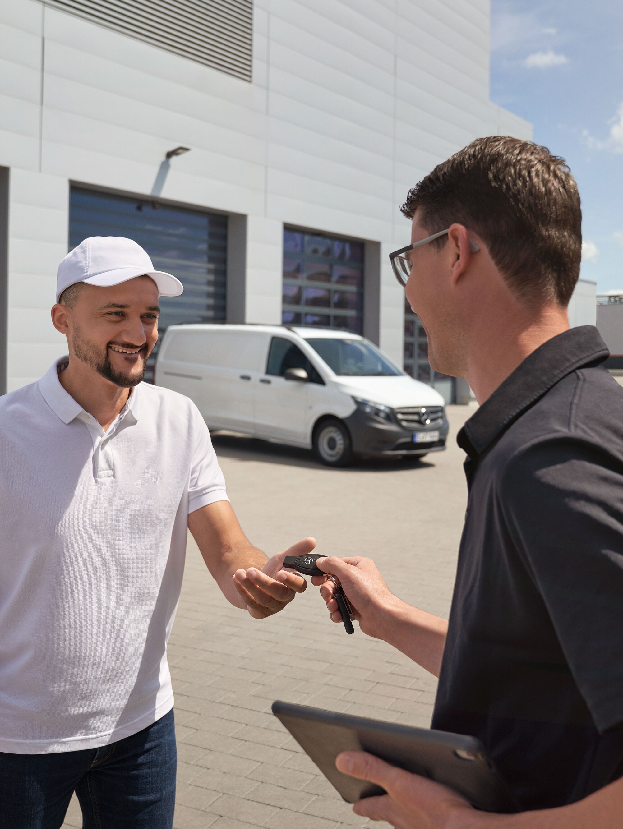 Mercedes-Benz servicemedewerker overhandigt sleutels aan een klant met een witte Mercedes-Benz Vito bestelwagen op de achtergrond.