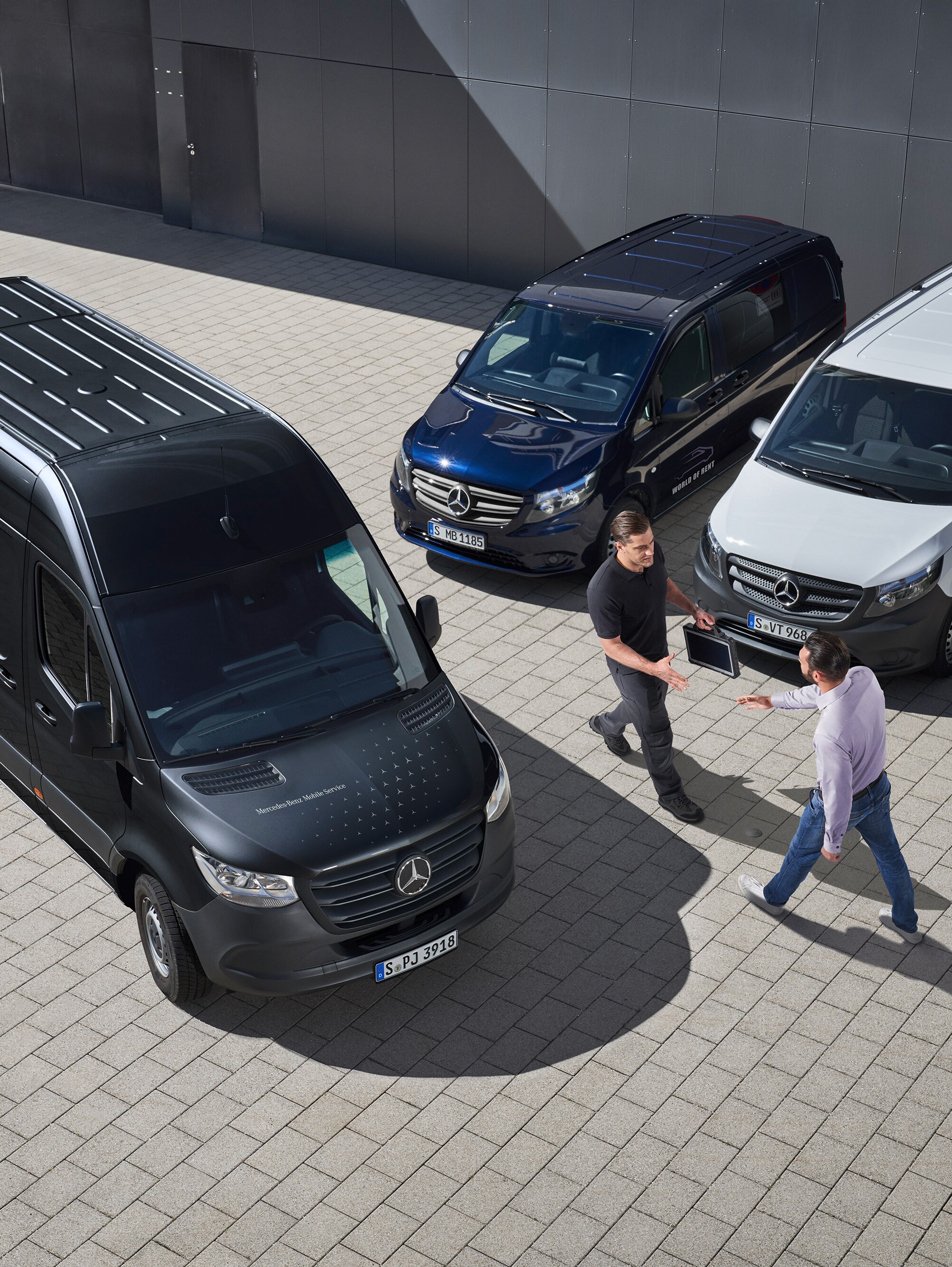 Twee mannen begroeten elkaar tussen Mercedes-Benz bestelwagens.