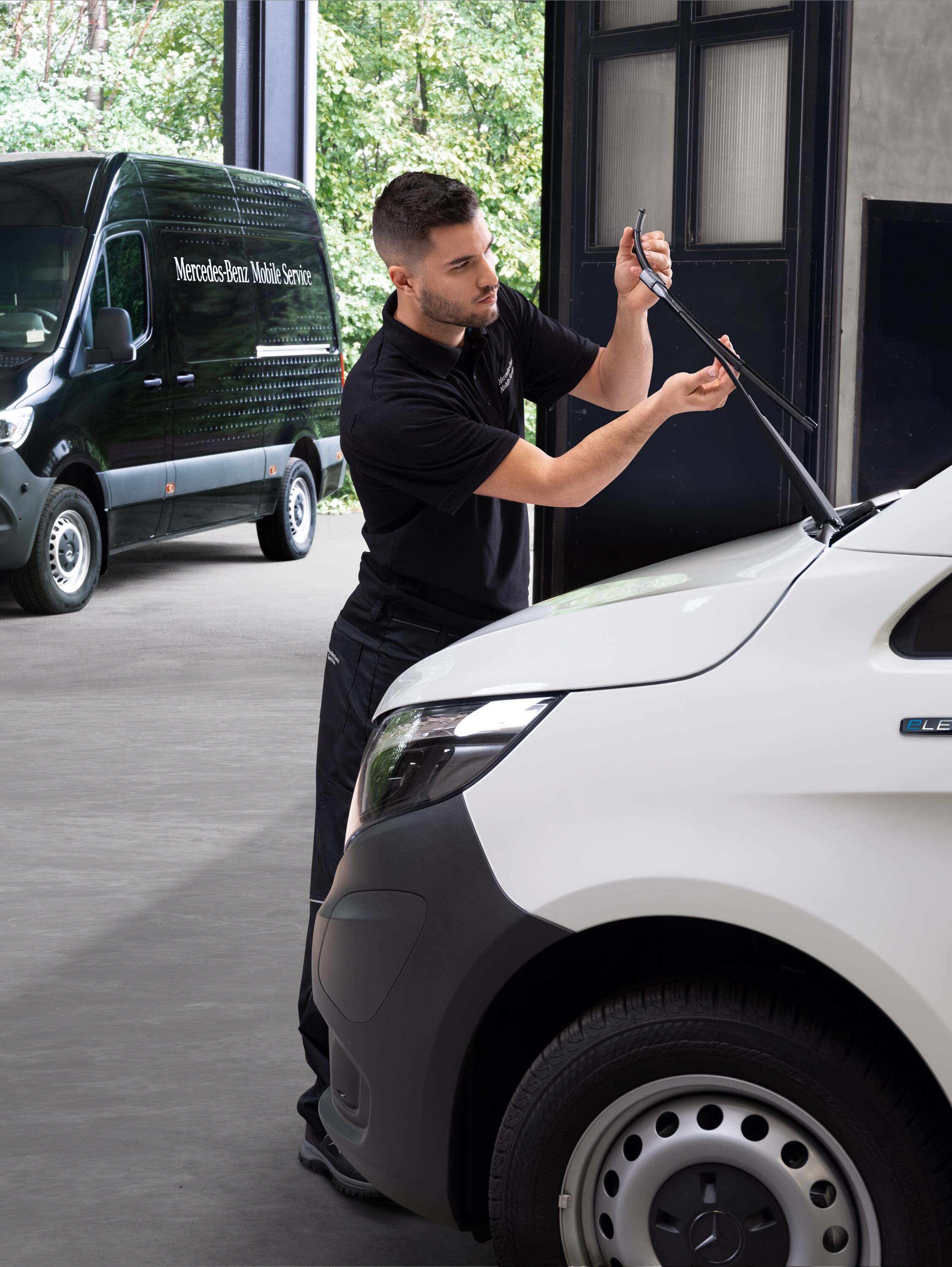 Een monteur vervangt ruitenwisserbladen op een witte Mercedes-Benz Vito Gesloten Bestelwagen.
