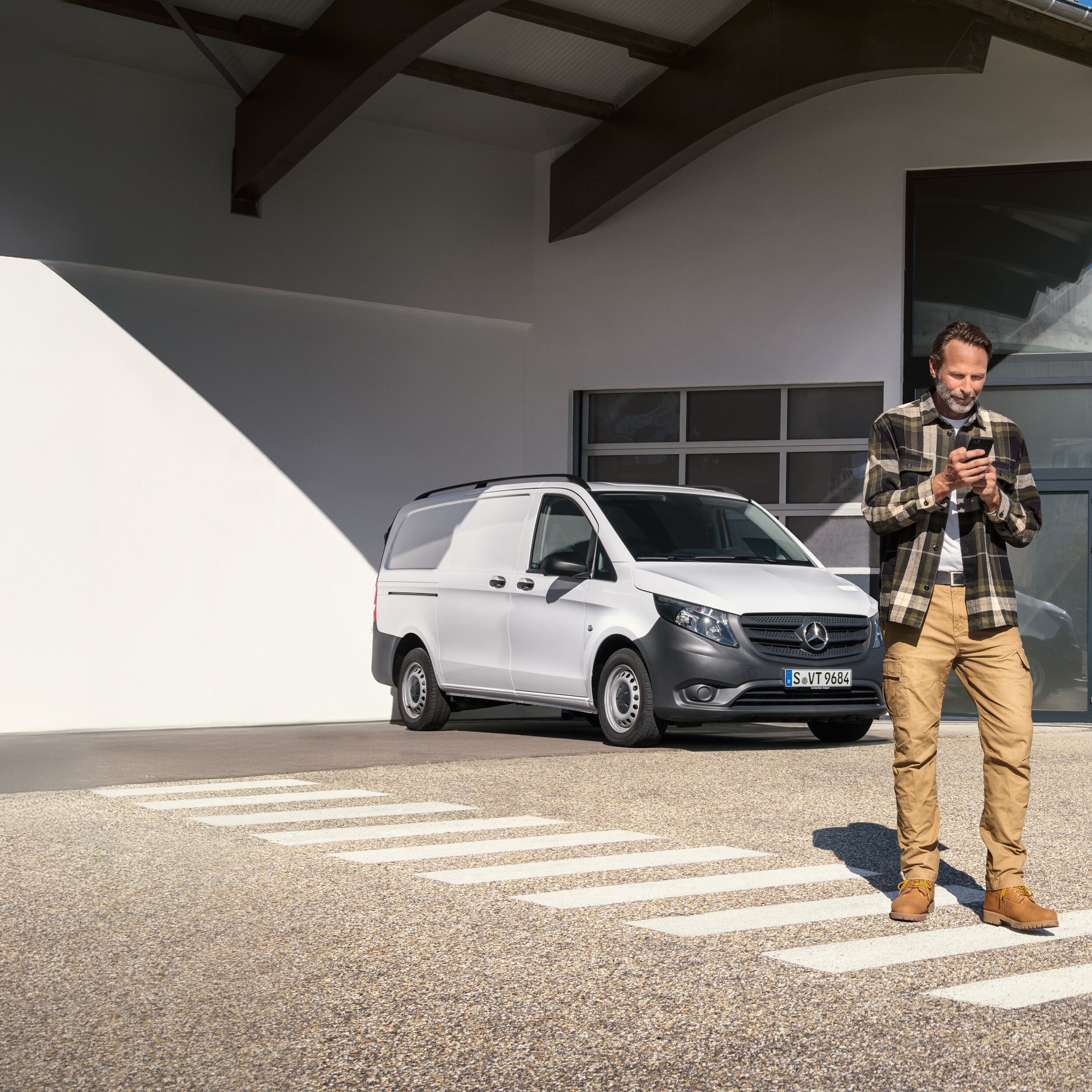 Een klant maakt via zijn mobiele apparaat een afspraak terwijl hij voor een witte Mercedes-Benz Vito-bestelwagen staat.