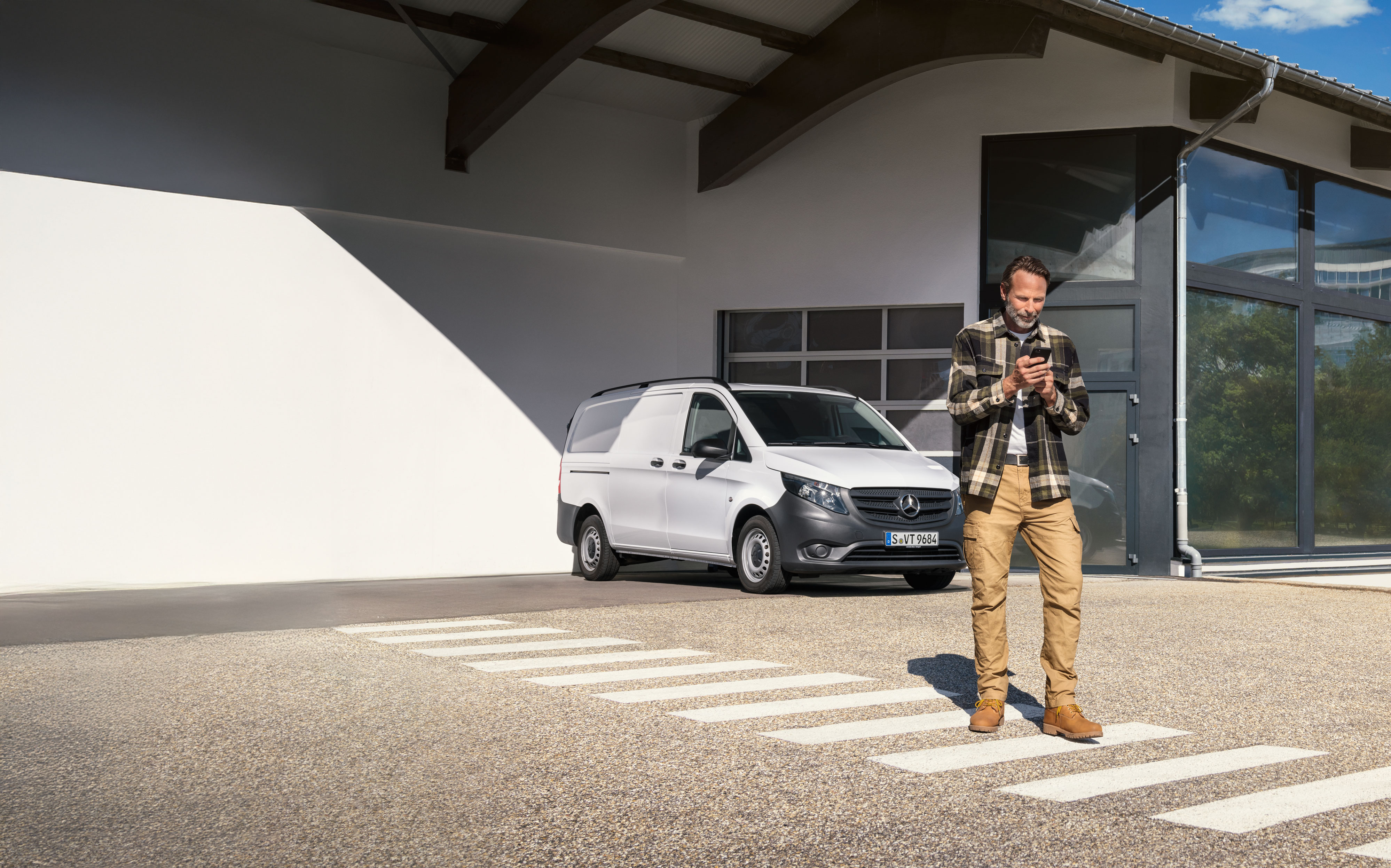 Mercedes-Benz | Onderhoud | Afspraak maken Een klant maakt via zijn mobiele apparaat een afspraak terwijl hij voor een witte Mercedes-Benz Vito-bestelwagen staat.