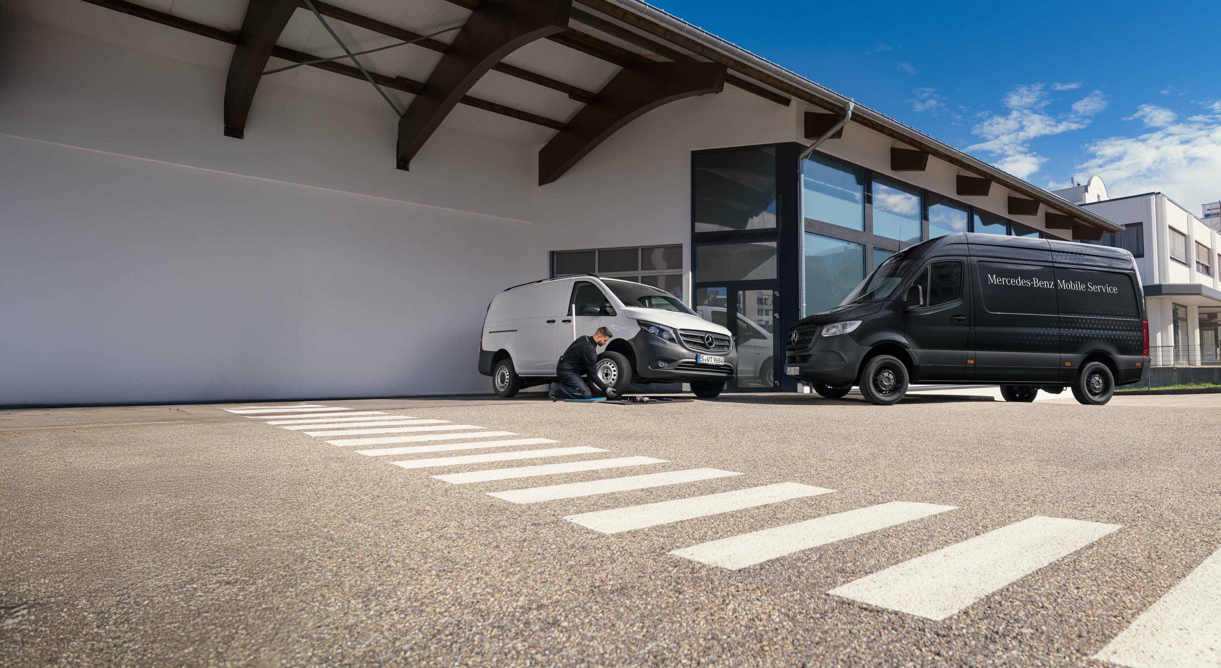 Mercedes-Benz Bedrijfswagen | Mobiele Service | Service Aanvragen Technicus vervangt een band van een witte Mercedes-Benz Vito Bedrijfswagen op een parkeerterrein.